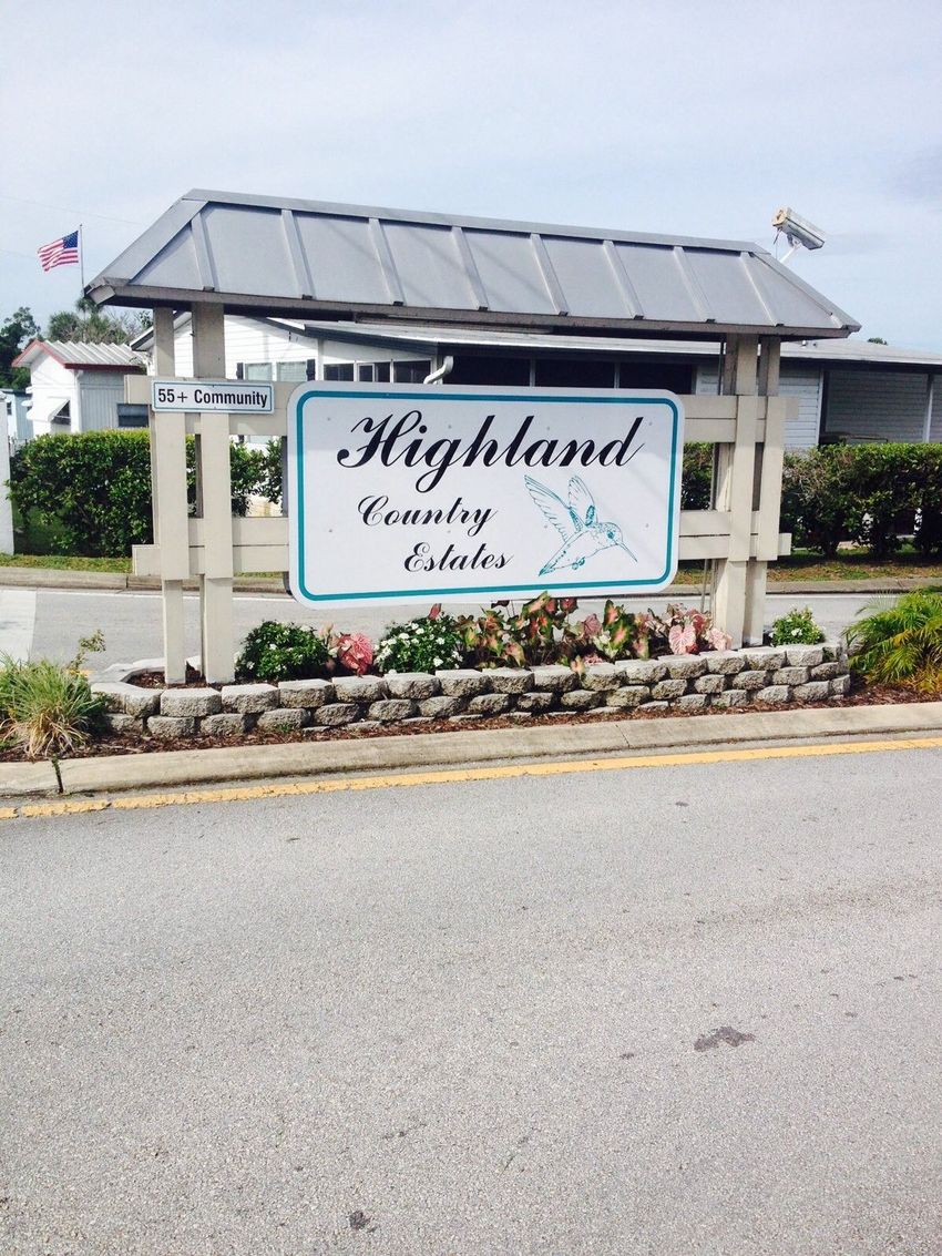 Entrance sign for Highland Country Estates beside a road, with flowers and stone landscaping.