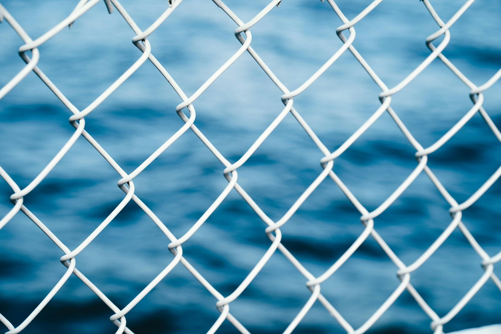 White chain-link fence with blue water in the background
