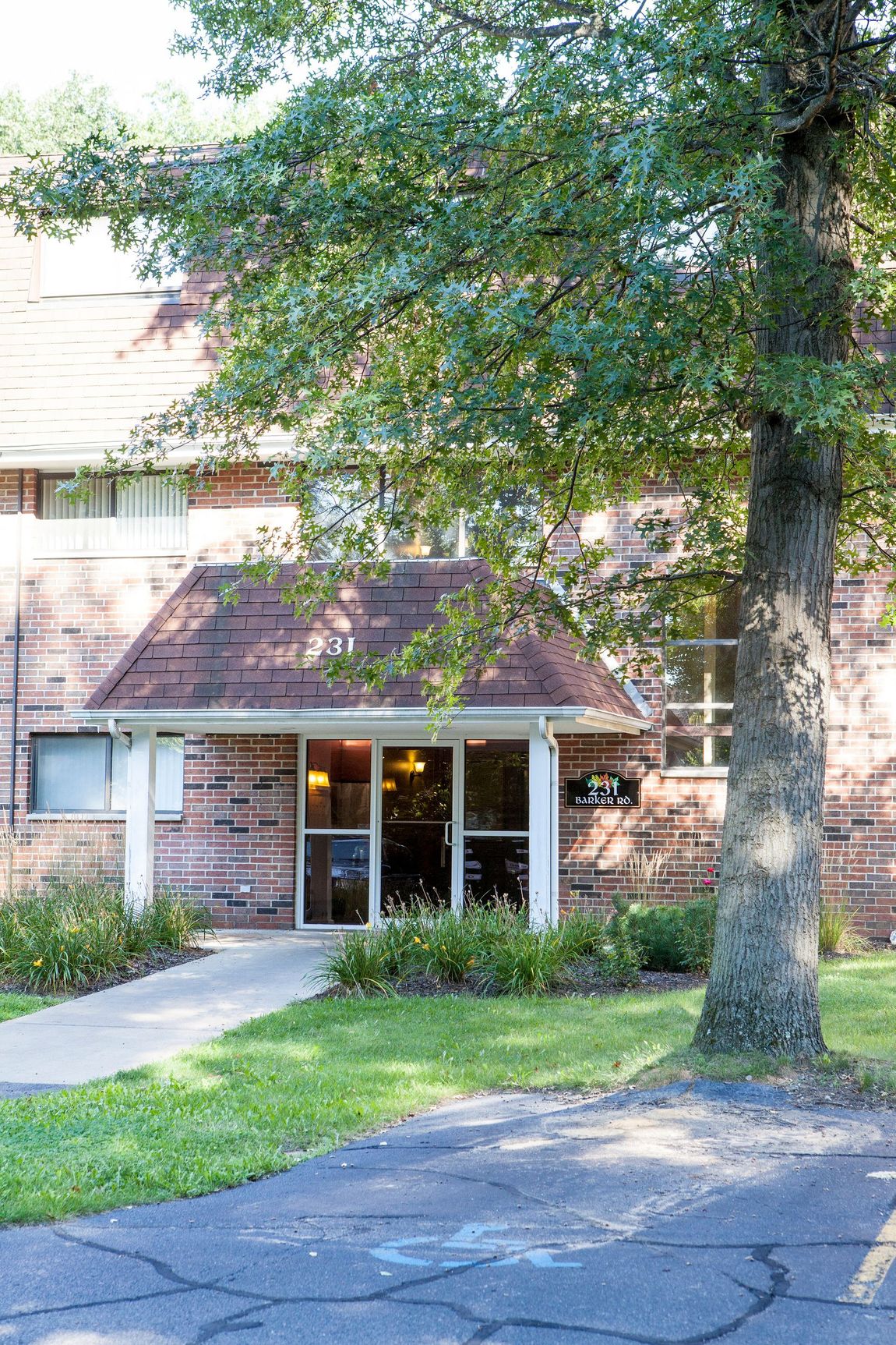 Brick building with a covered entrance, a tree to the right, and a sidewalk.