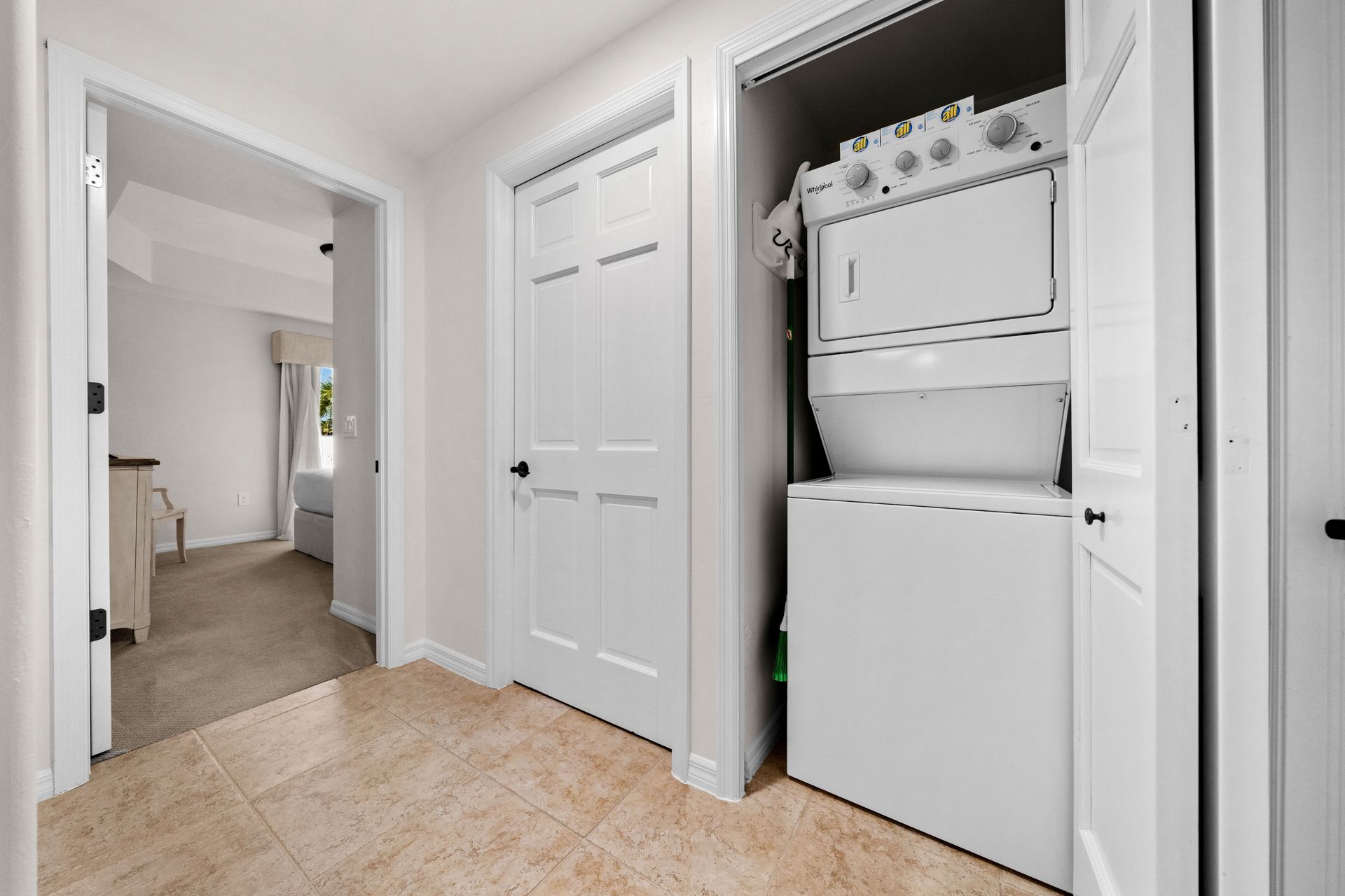 Bright hallway with white doors and a laundry closet containing a stacked washer and dryer.
