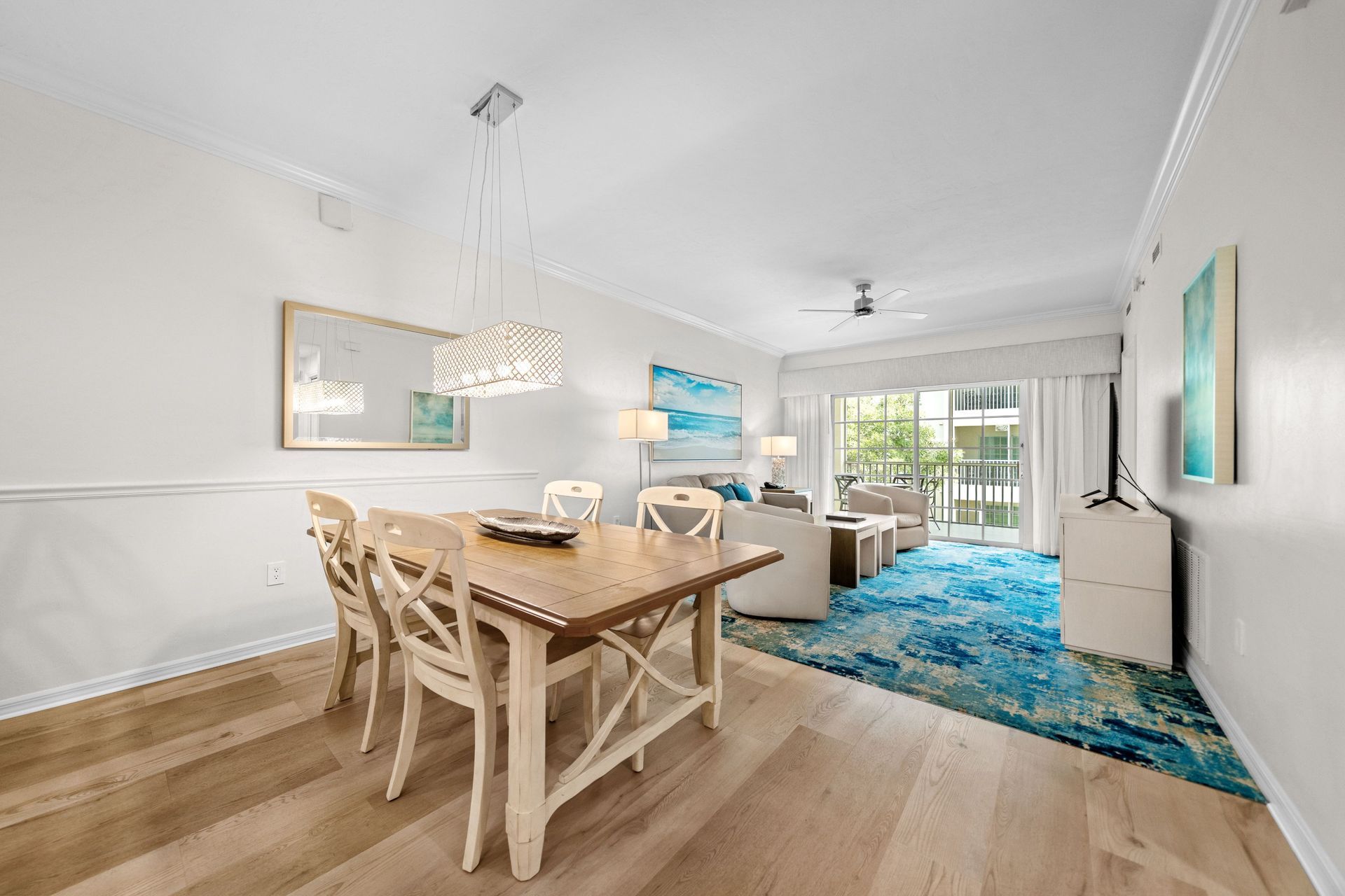 Bright dining and living room with white furniture, blue rug, and balcony view