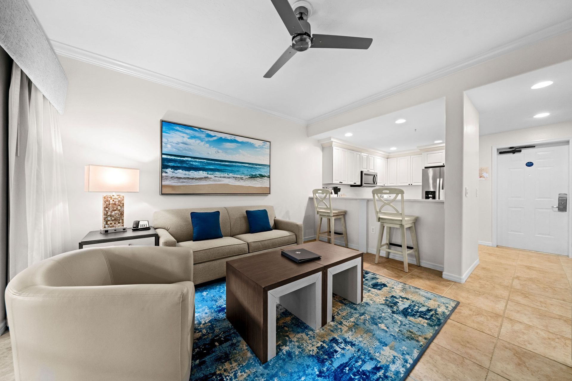Modern living room with beige sofa, blue rug, wall art, and open kitchen area