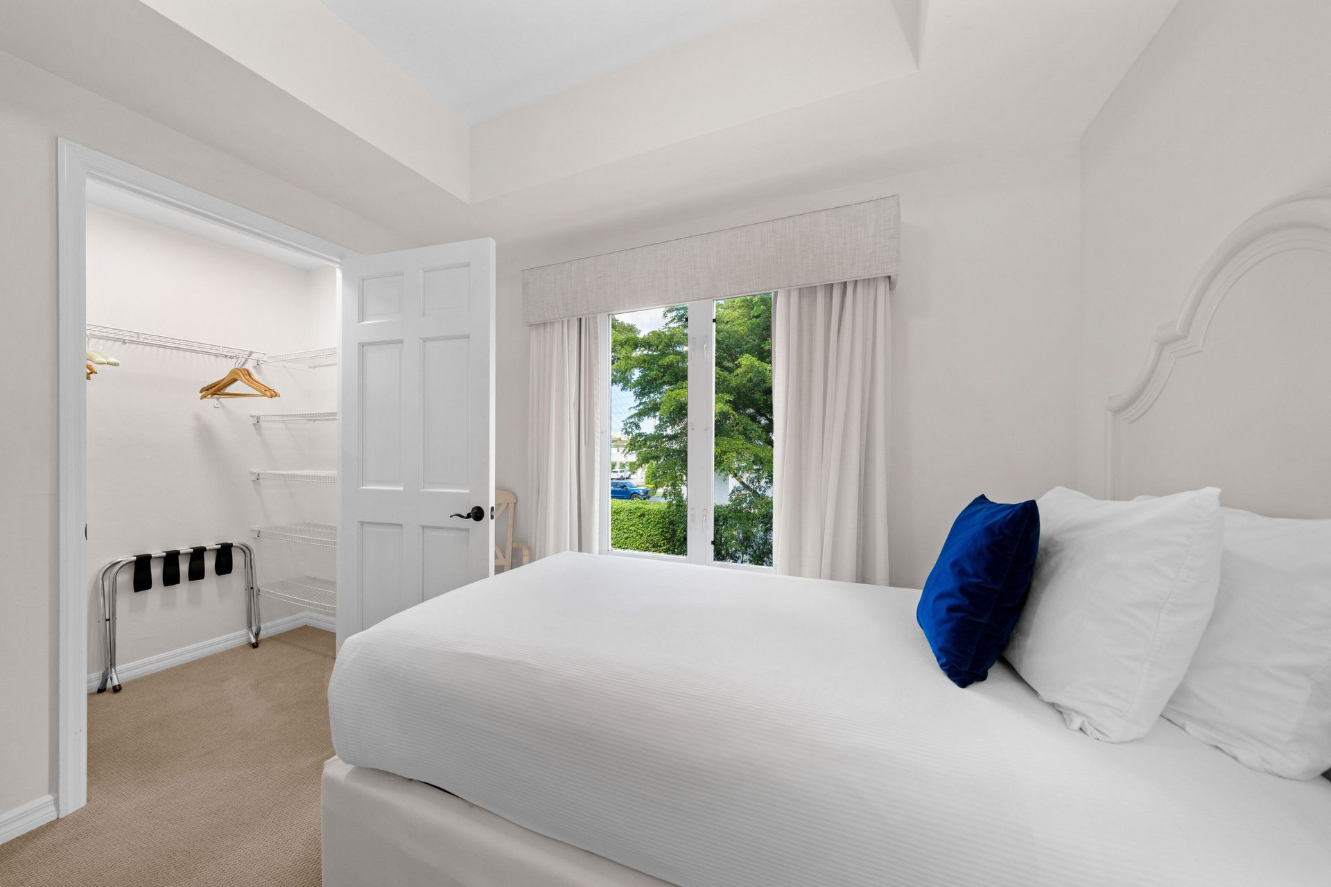 Bright white bedroom with a bed, blue accent pillow, window, and open closet area
