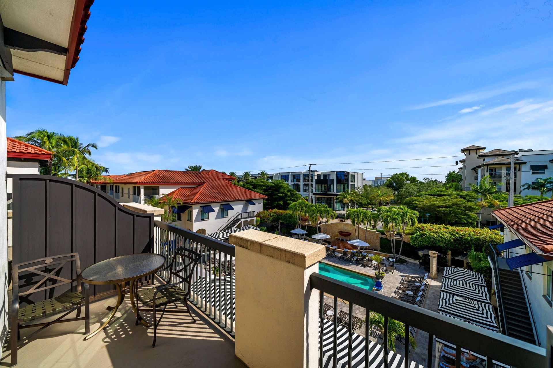 Balcony view over rooftops and a turquoise pool under a bright blue sky