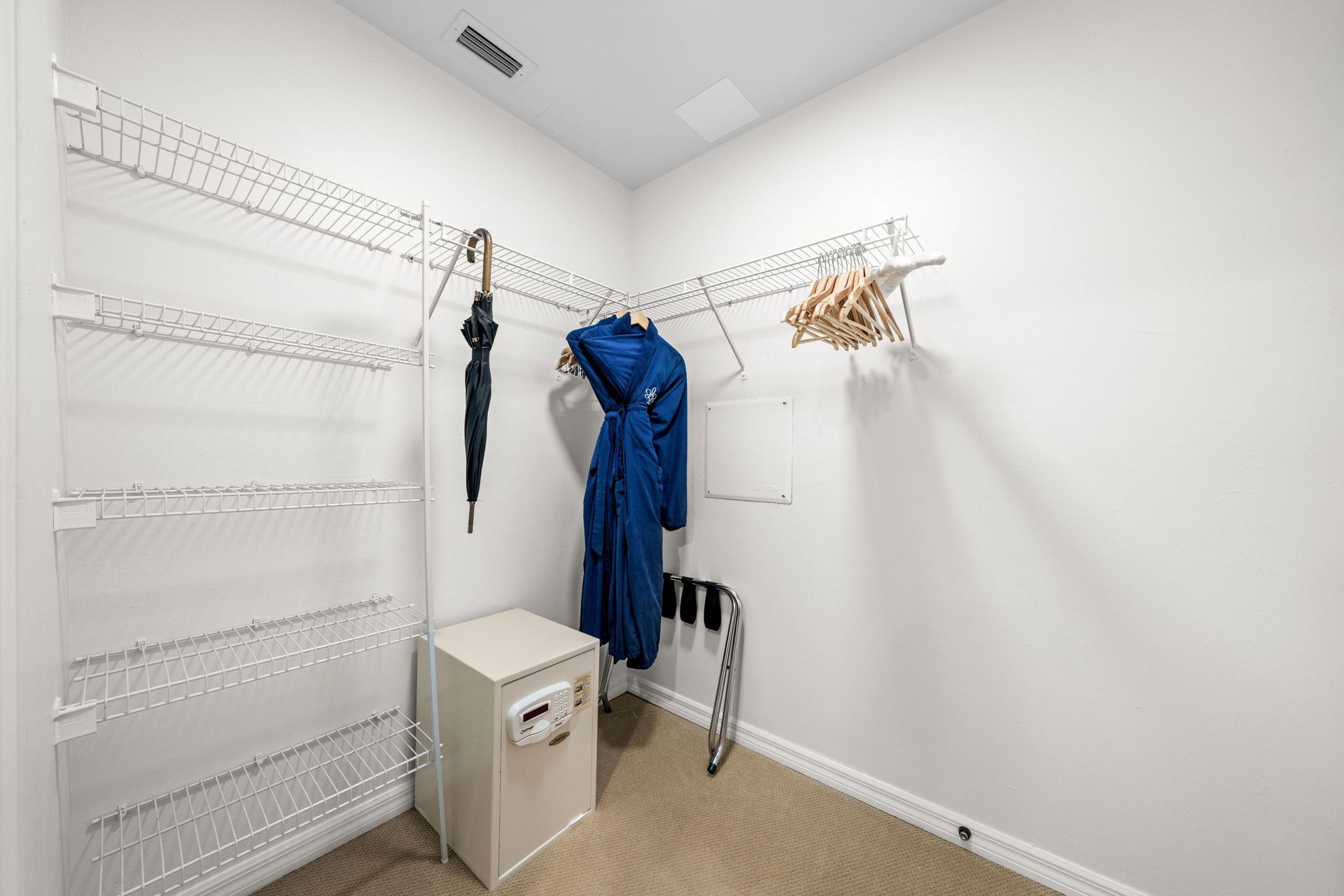 White locker room corner with wall hooks, hanging coats, a small cabinet, and a cane on the floor