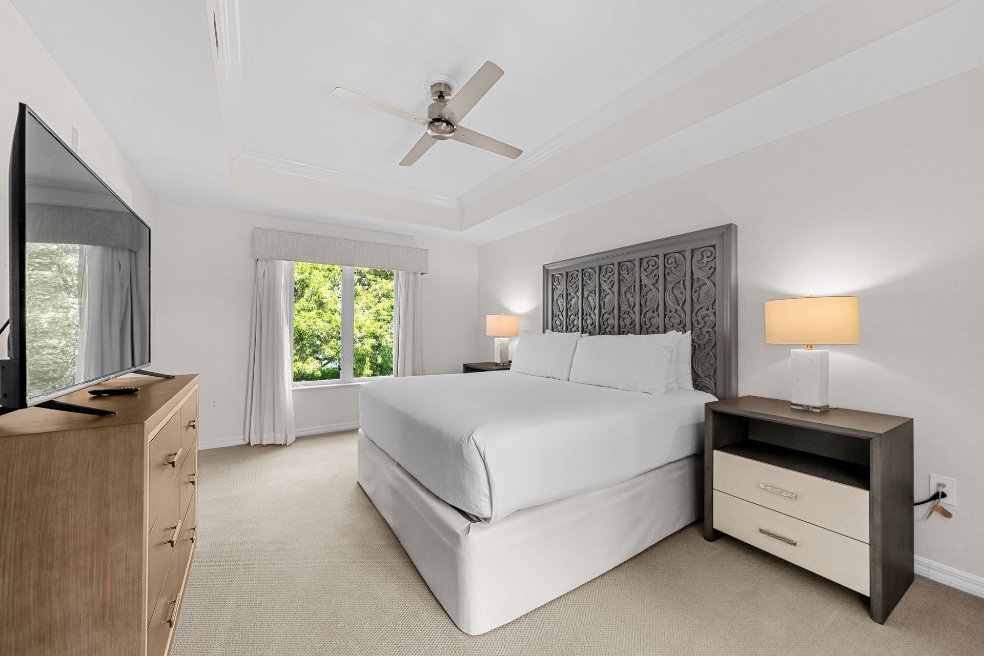 Bright modern bedroom with king bed, dresser, nightstands, ceiling fan, and balcony doors