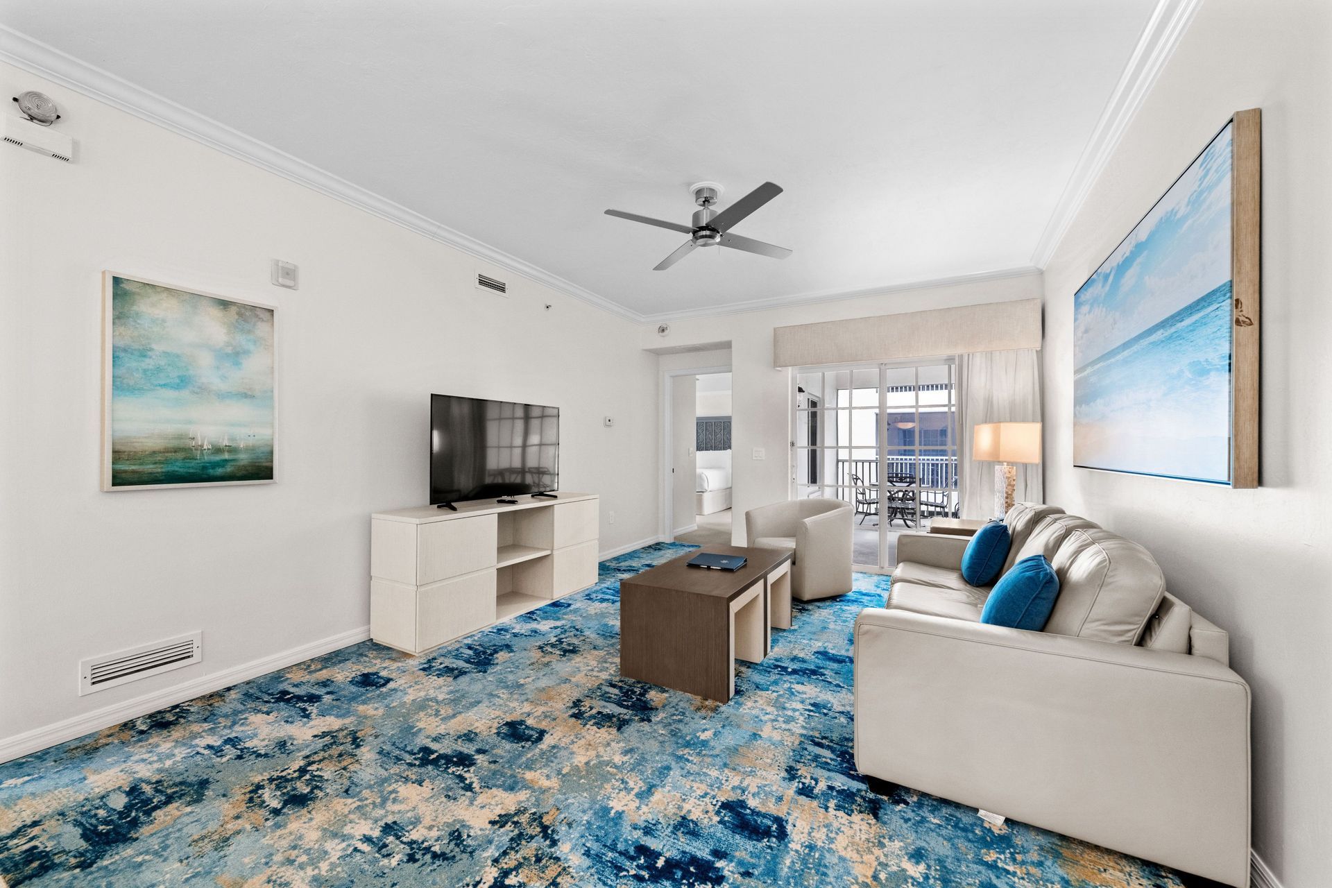 Bright modern living room with white sofa, blue rug, wall art, TV, and ceiling fan