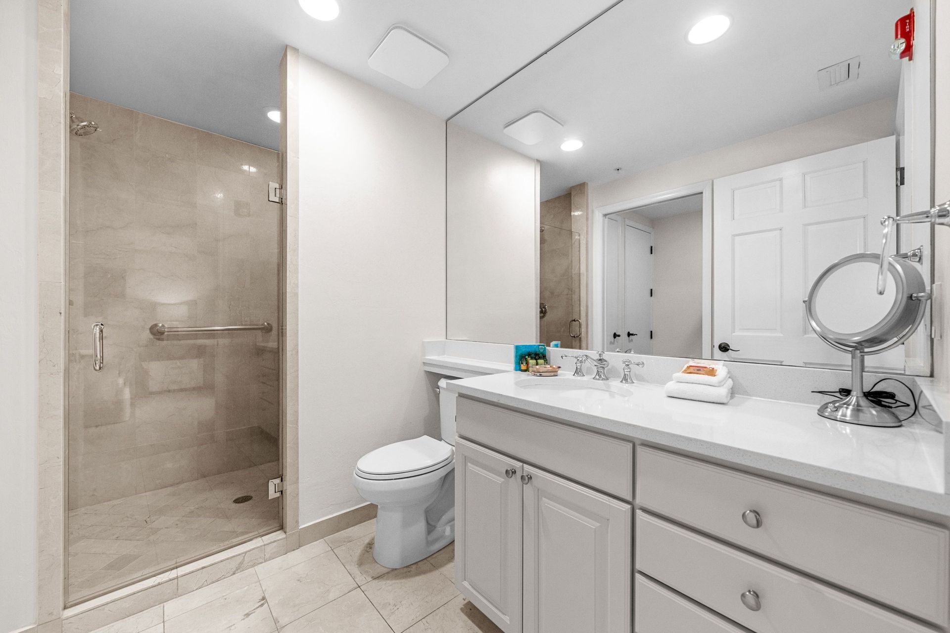 Bright modern bathroom with walk-in shower, white vanity, toilet, and large mirror.