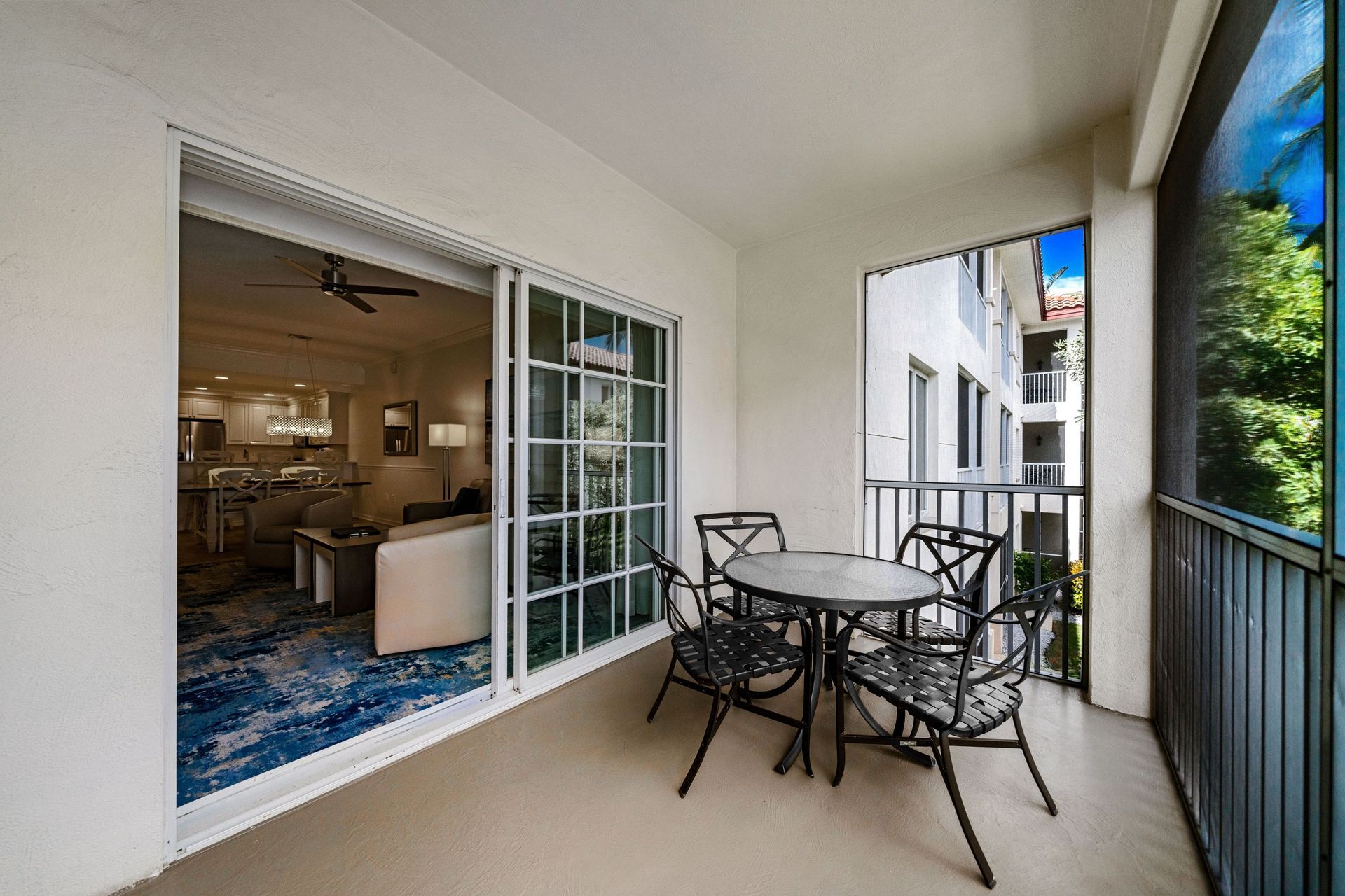 Covered balcony with metal patio table and chairs beside a sliding glass door.