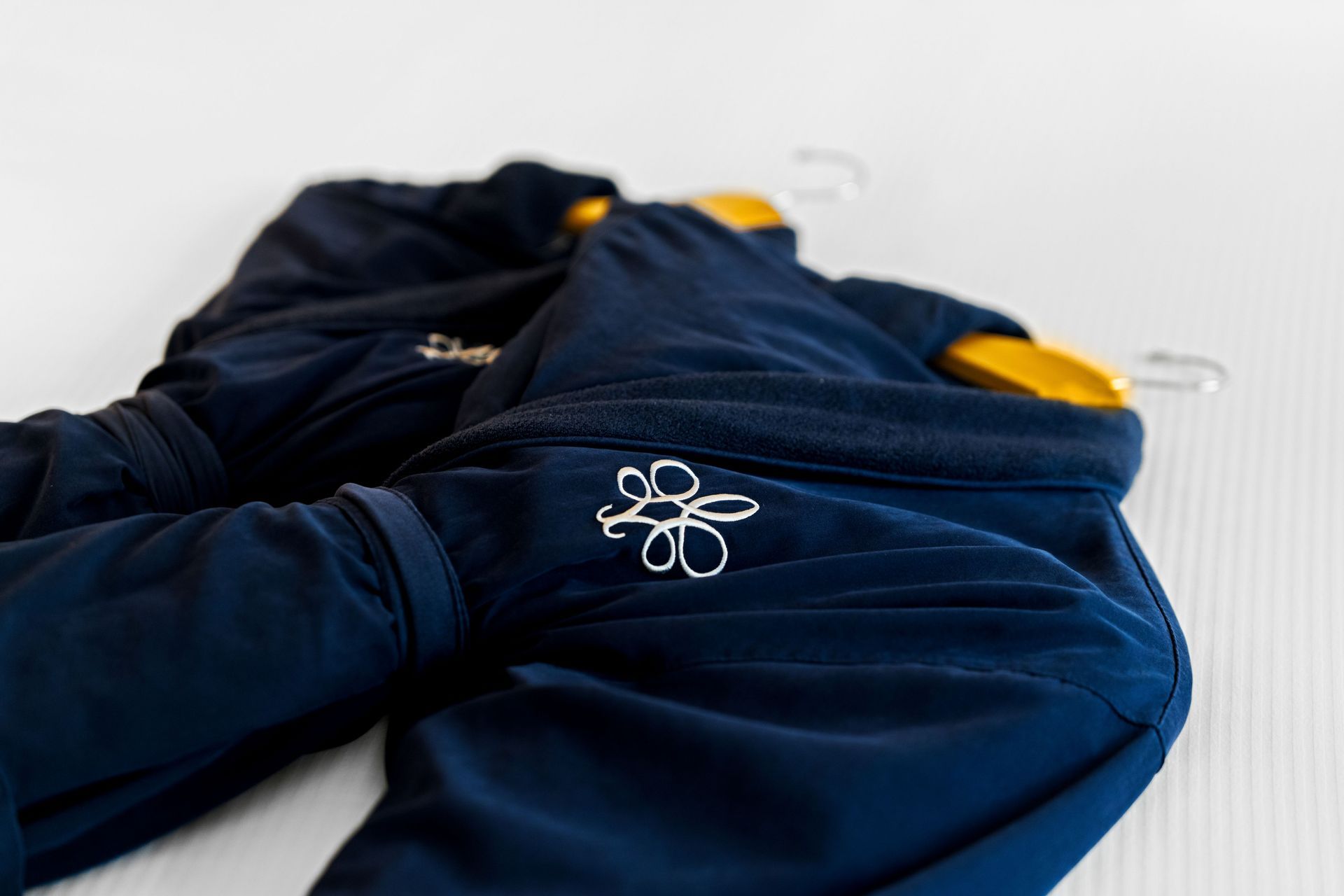 Dark navy jacket with yellow accents and a white flower logo, lying on a light surface.