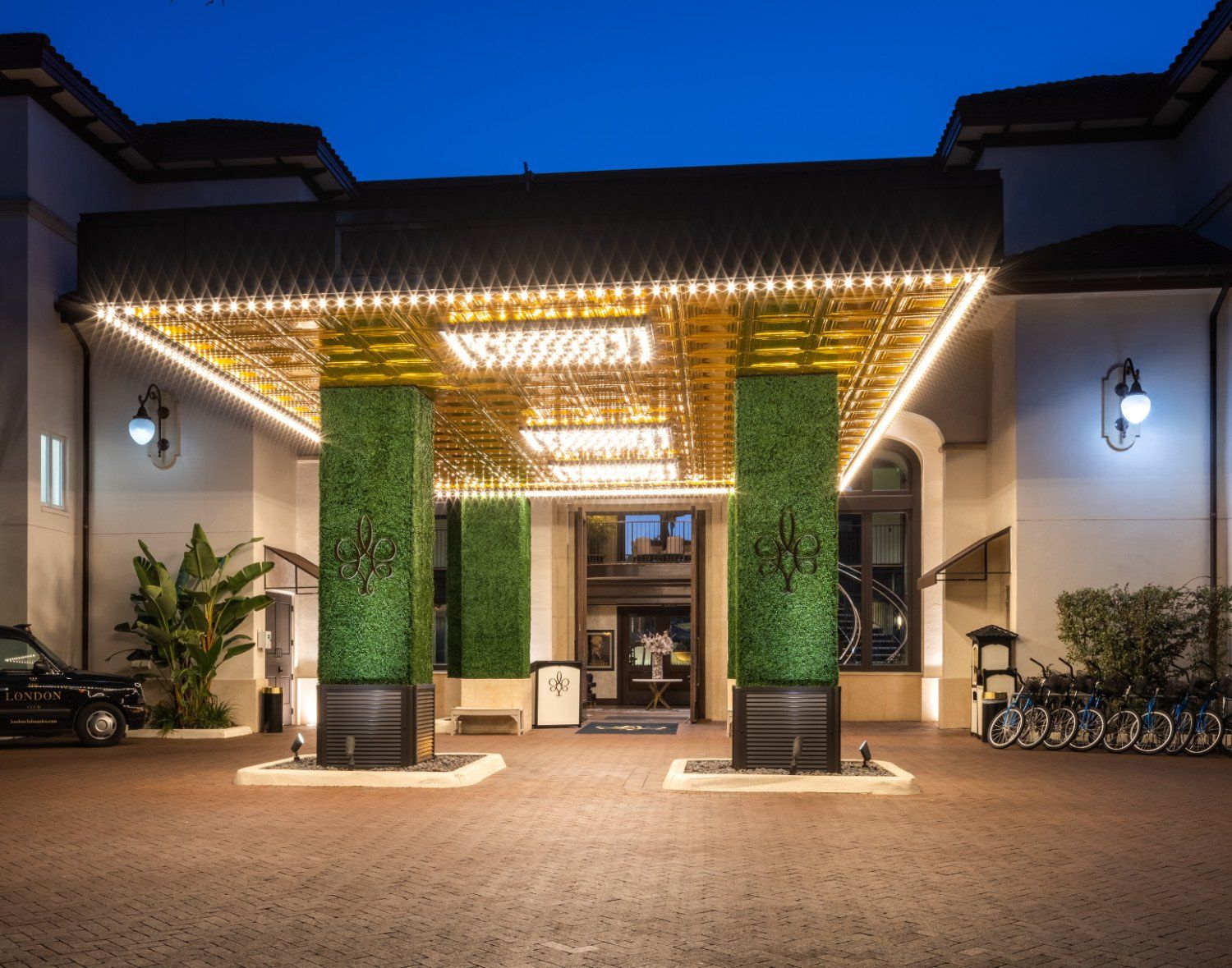 Illuminated building entrance at night with green vertical planters and warm string lights.