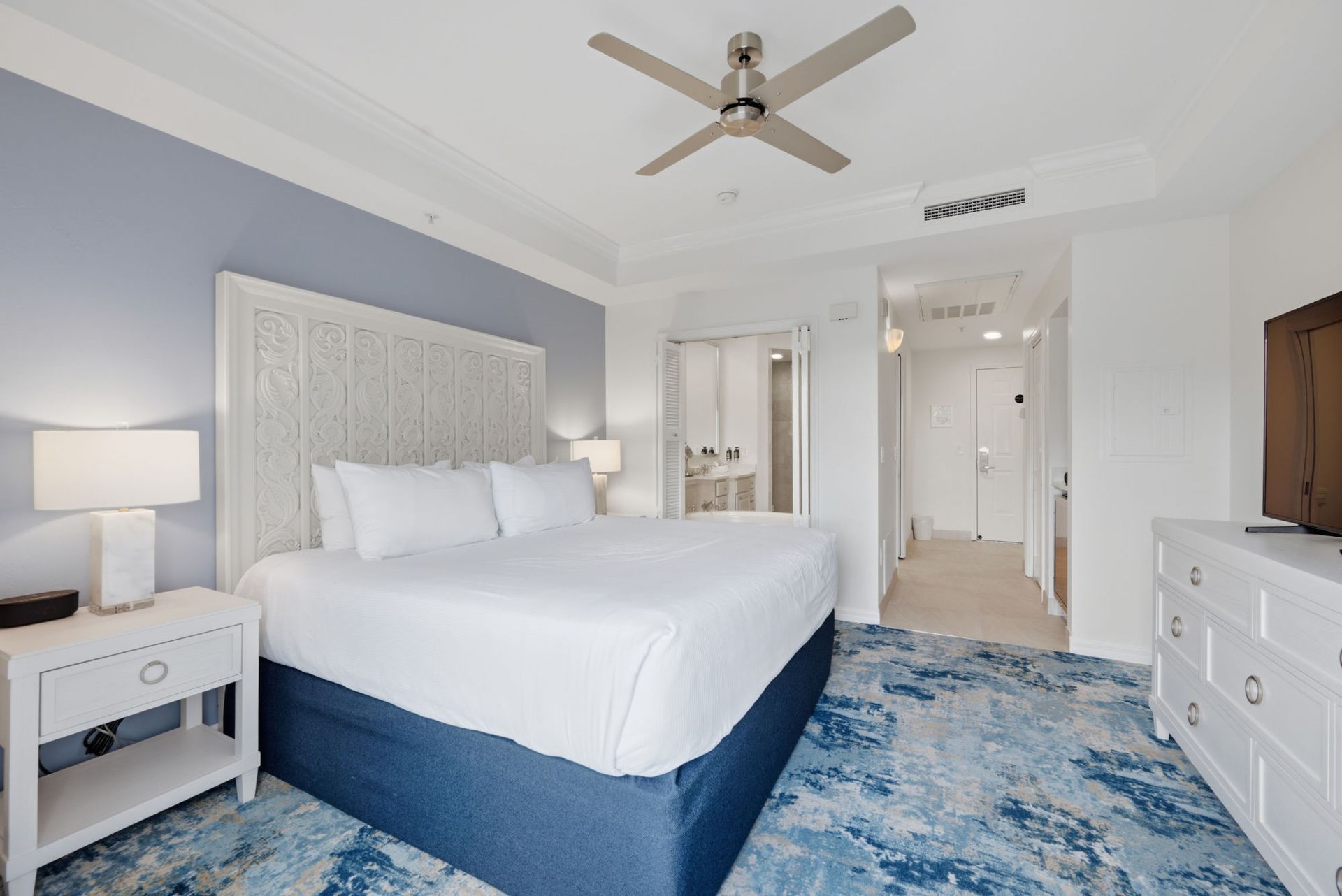 Bright bedroom with a king bed, blue rug, and balcony doors with ocean view