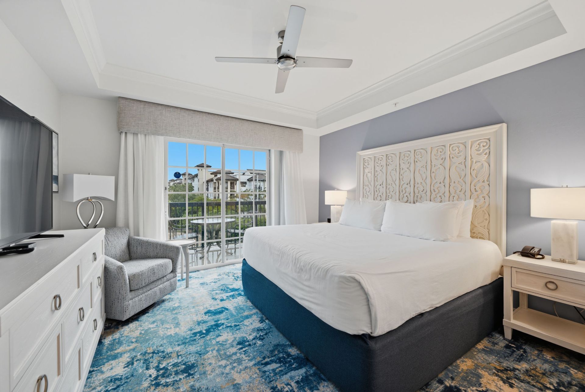 Bright bedroom with a large bed, TV on dresser, balcony doors, and ceiling fan