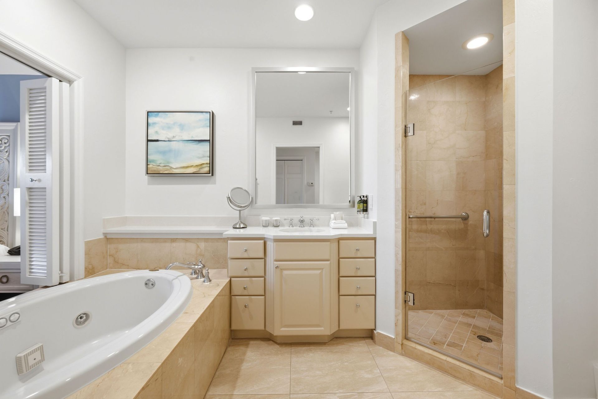 Bright bathroom with a large oval bathtub, marble counters, and a view into a sunlit bedroom.