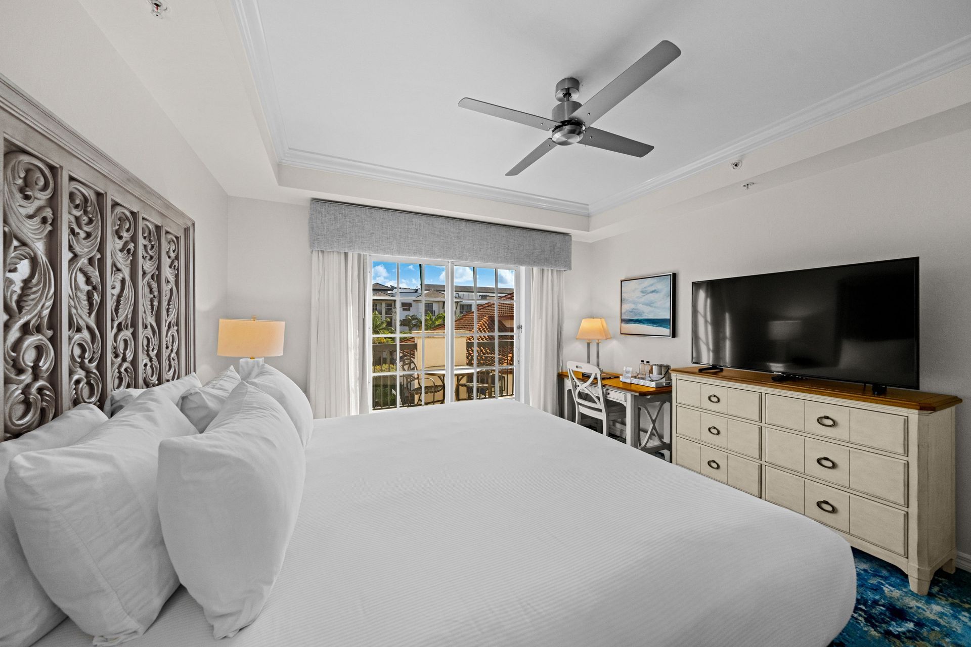 Bright bedroom with a large bed, TV on dresser, balcony doors, and ceiling fan
