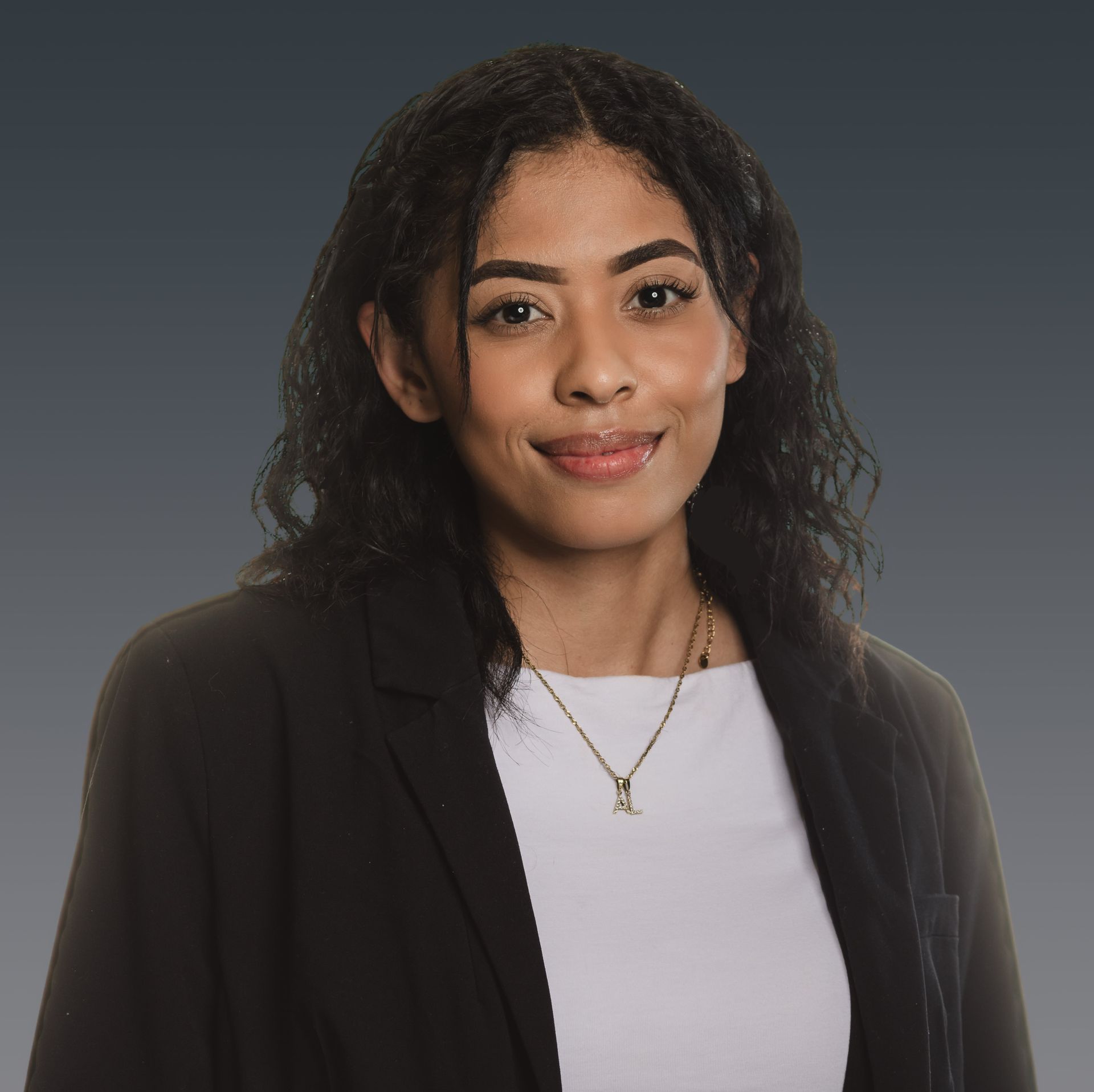 Portrait of a smiling person in a black blazer and white top against a gray background