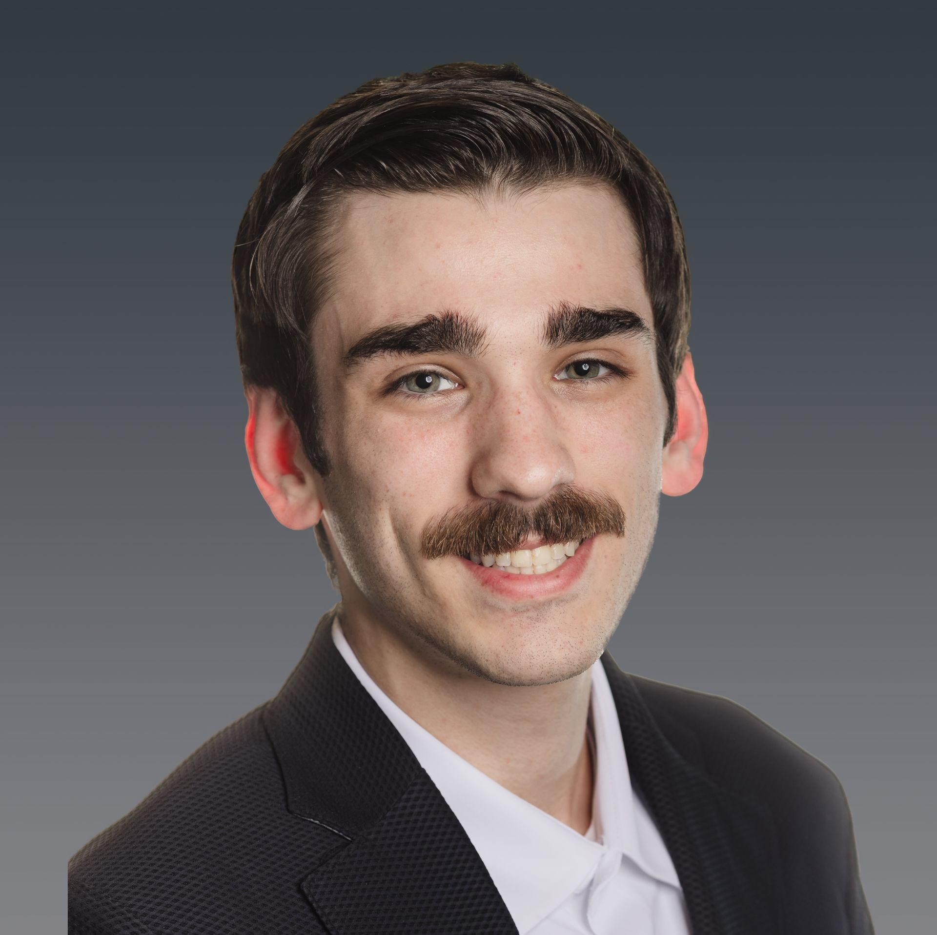 Portrait of a smiling man with dark hair and a mustache in a dark suit against a gray background