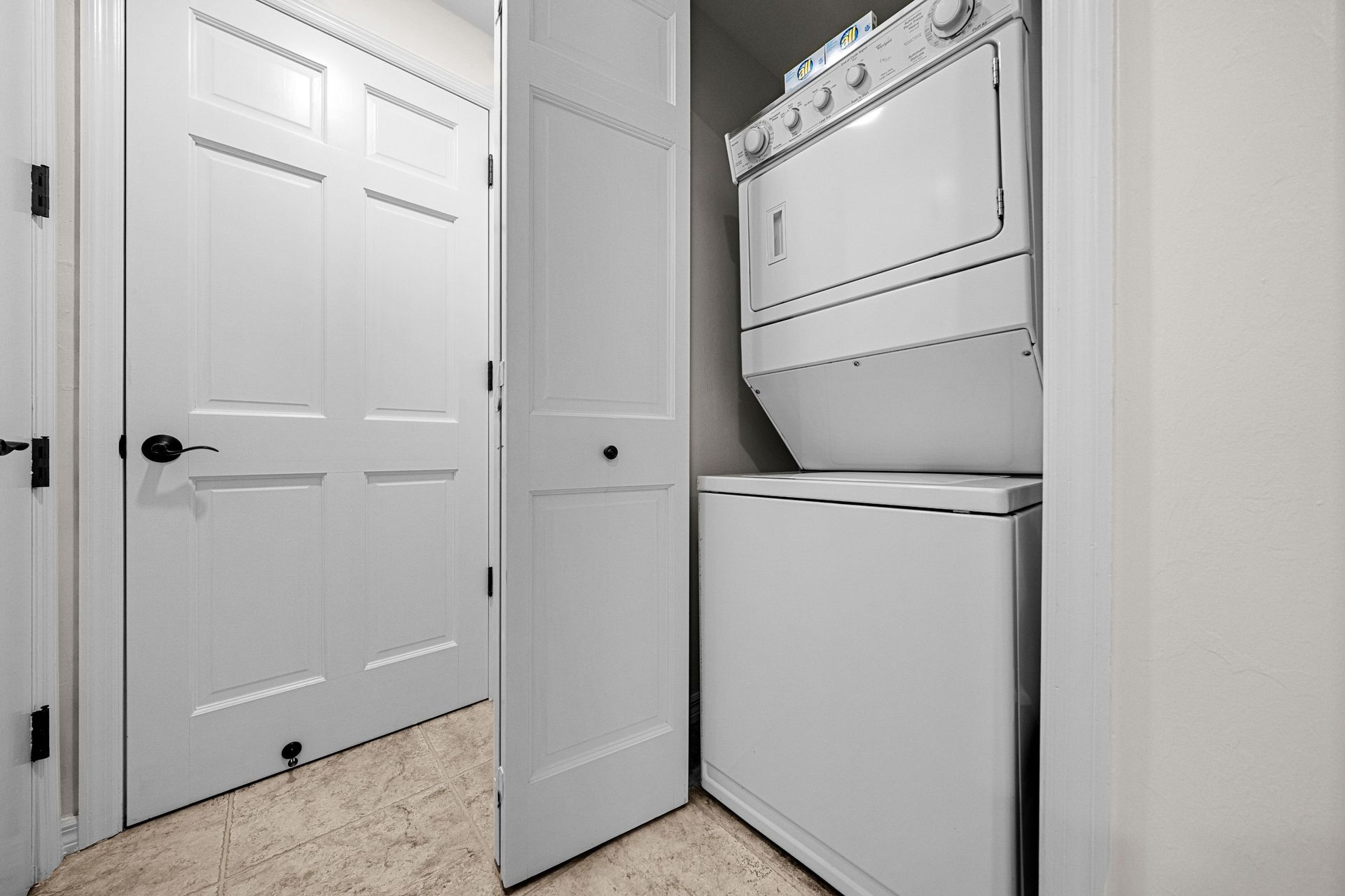 Laundry closet with stacked washer and dryer beside white louvered doors in a hallway