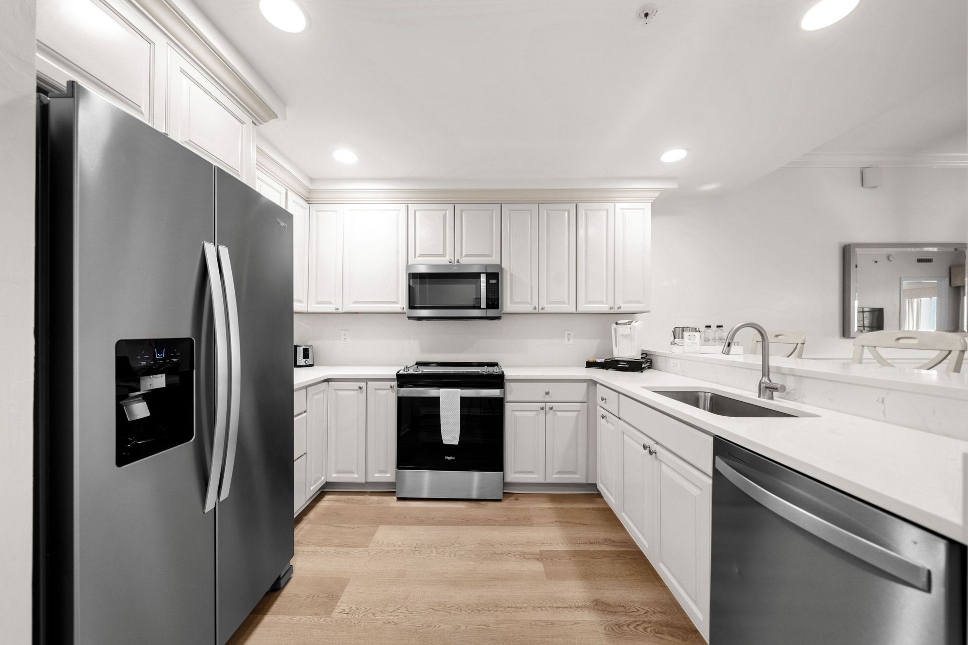 Bright modern white kitchen with stainless steel appliances and wood flooring