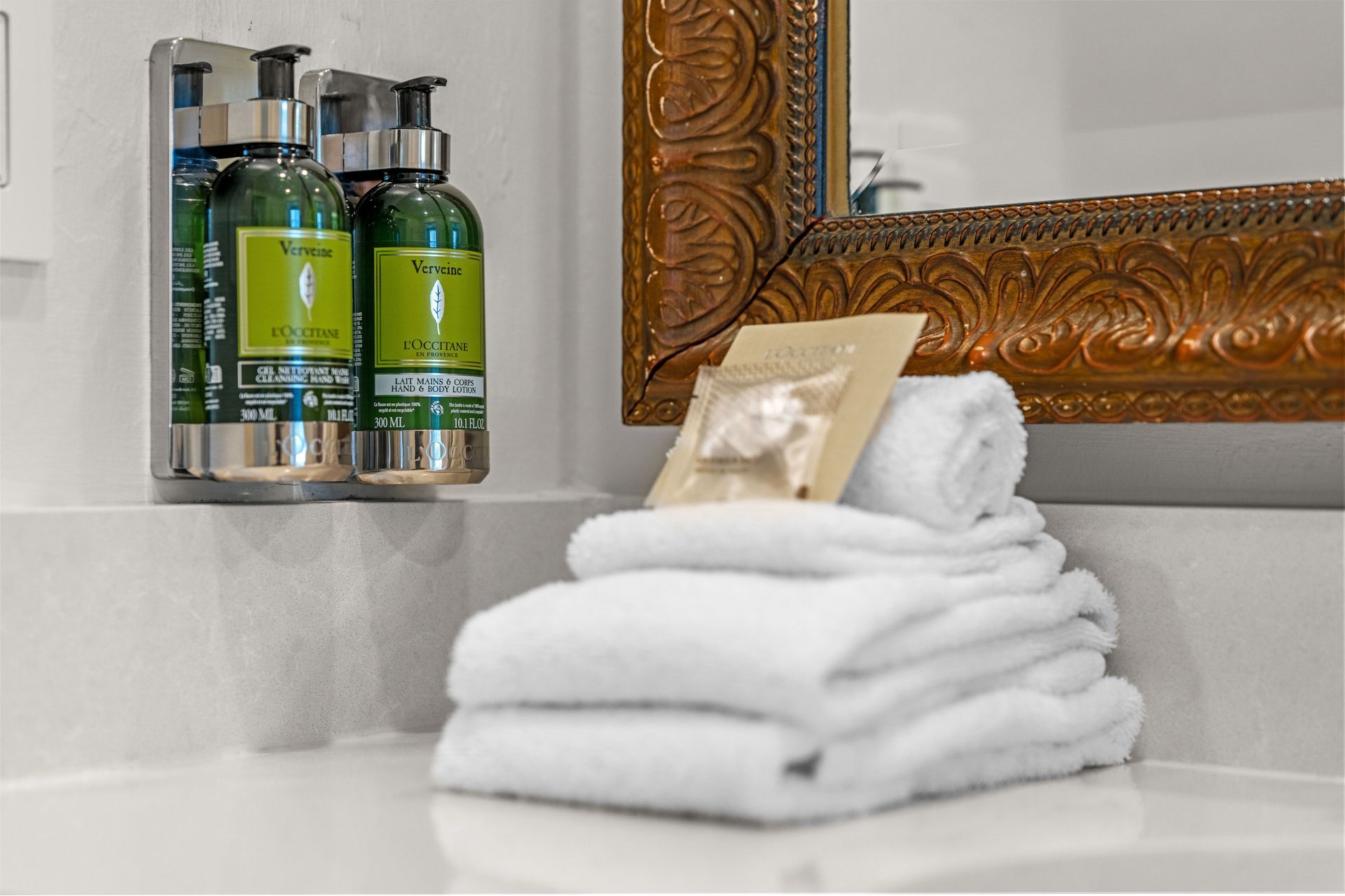 Stacked white towels with a soap bar on a bathroom counter beside green toiletries and a mirror