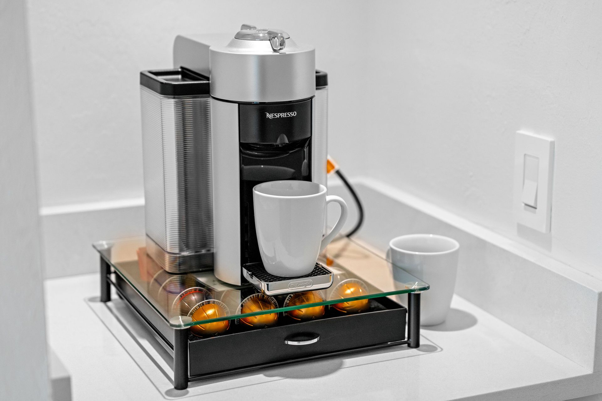Coffee maker on a kitchen counter with a cup and small tray of capsules inside a black frame