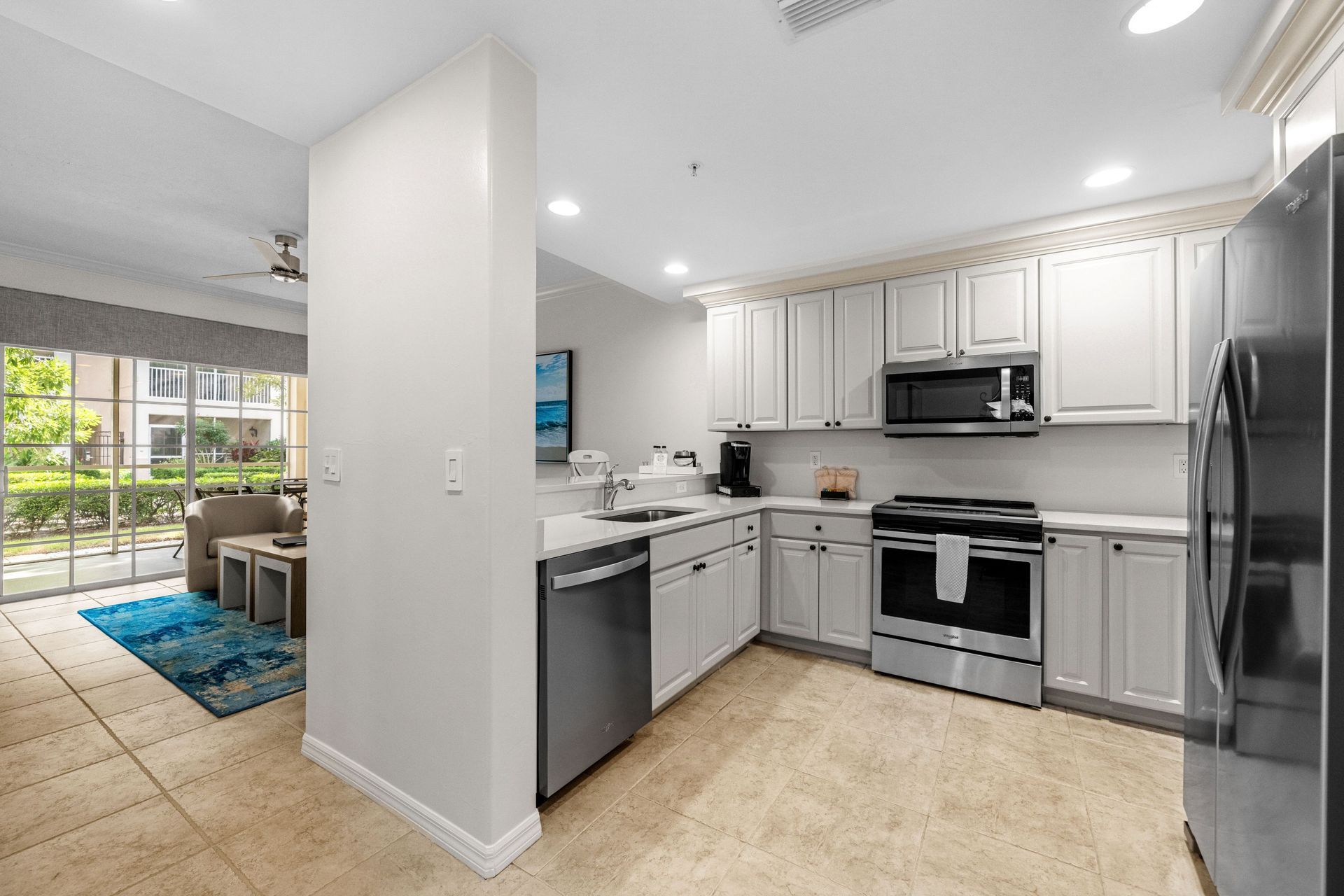 Bright white kitchen with stainless appliances, gray cabinets, and a view into a dining area.
