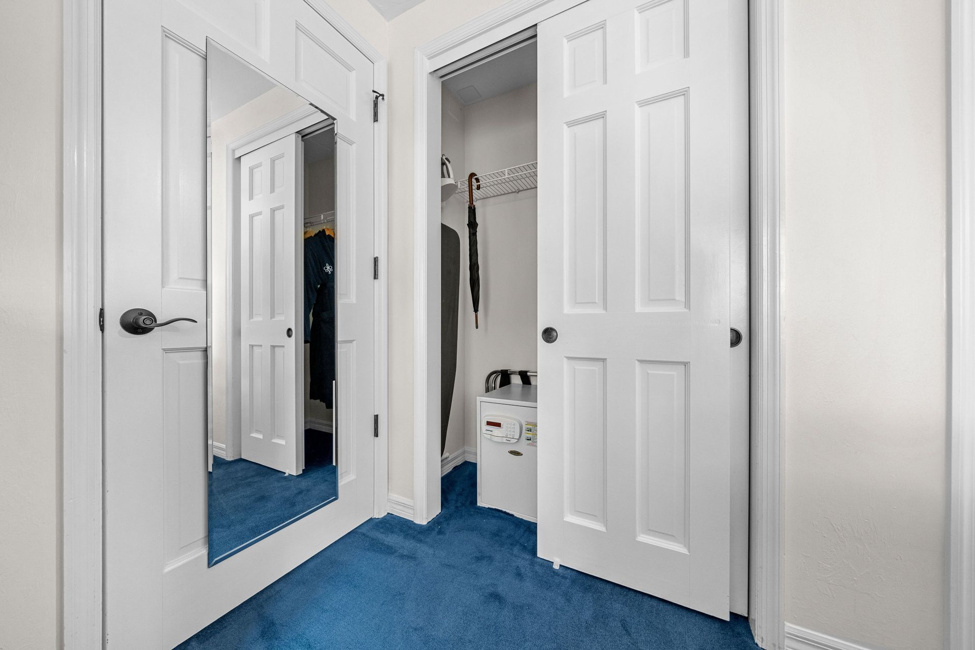 Bright hallway with blue carpet, white doors, and an open closet mirror.