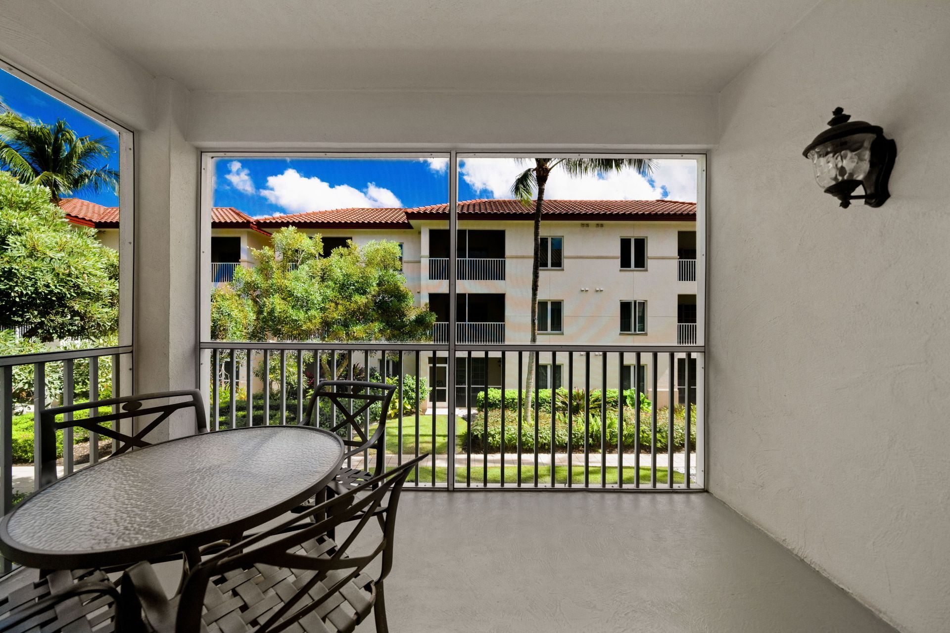 Covered patio with table and chairs overlooking an apartment building and palm trees
