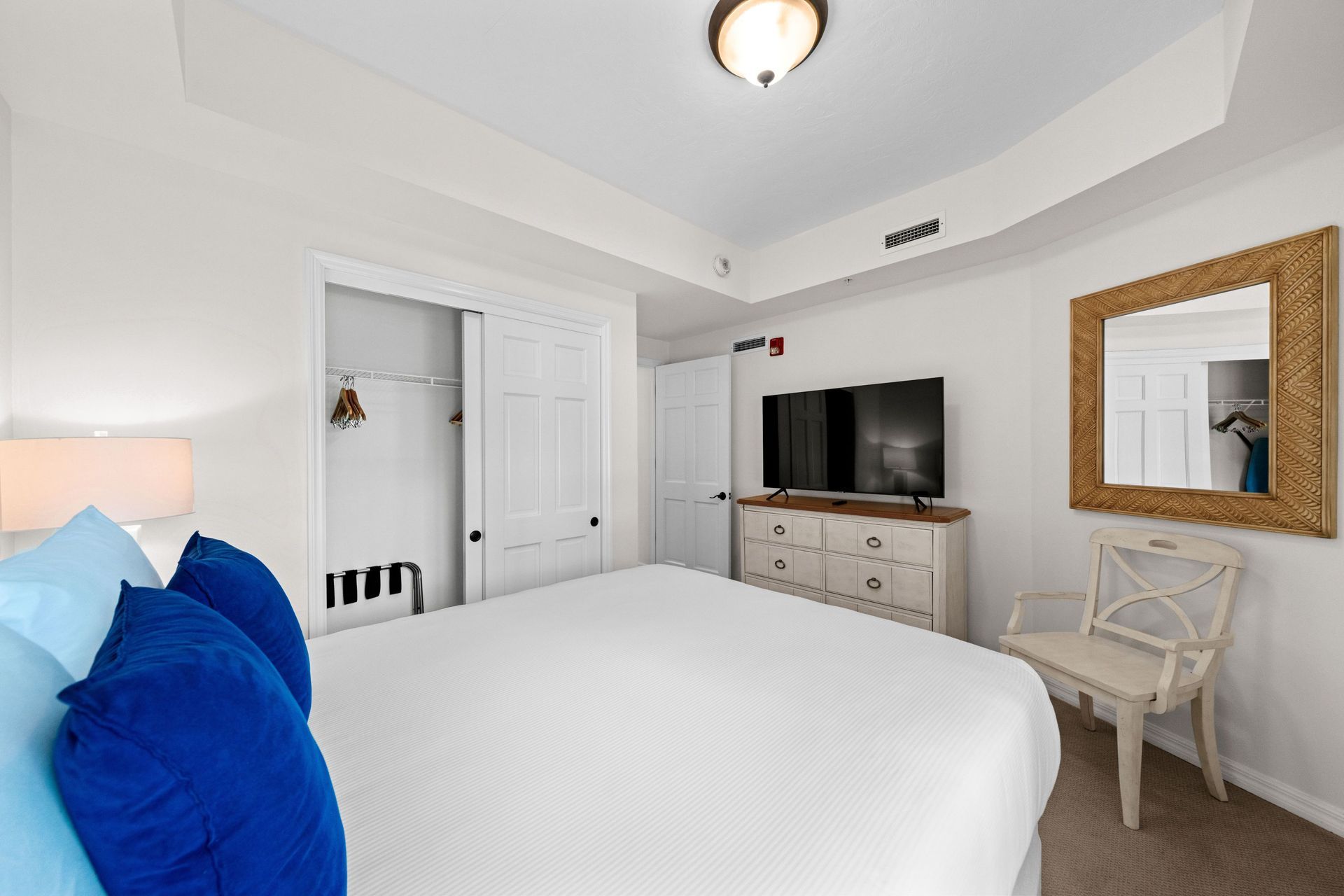 Bright white bedroom with blue pillows, a dresser TV, and a vanity mirror on the right