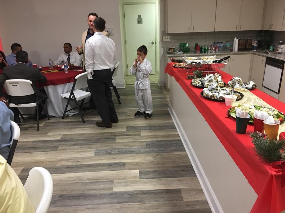 People at an event with food on a counter and tables. A child in pajamas stands in the middle.