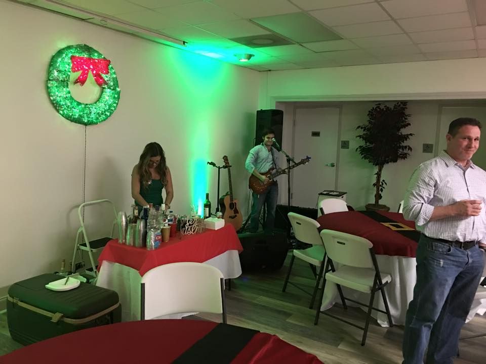 Christmas party: Bartender, musician, and guest in a room with green lighting. Red table cloths and a wreath.