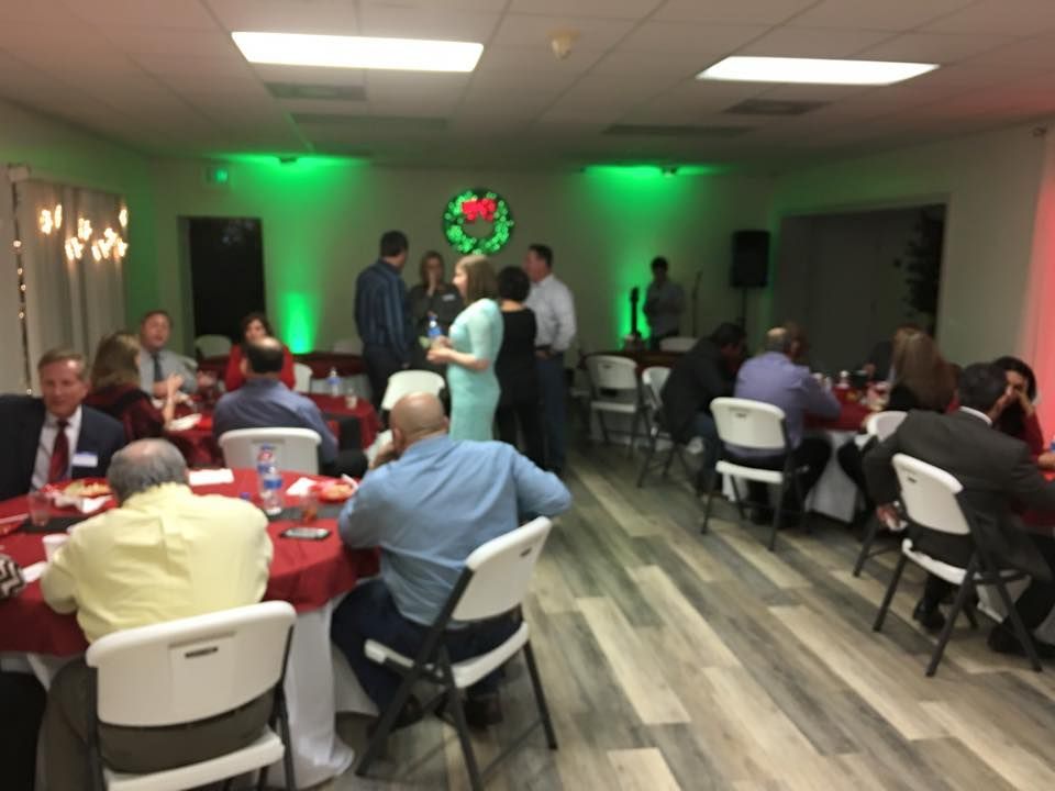 Holiday party in a decorated room with people socializing at tables. Green and red lighting.