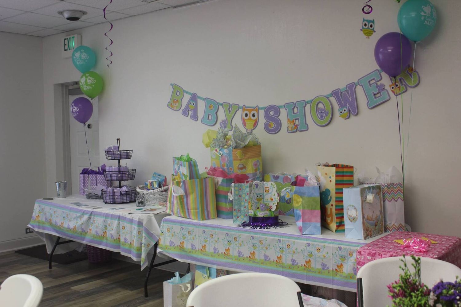 Baby shower with gifts and decorations. White walls, purple, green, and blue decor.