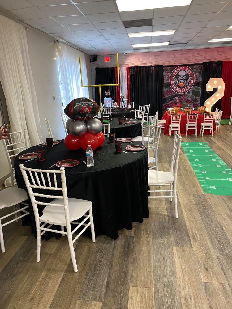 Football-themed party room. Round tables with black tablecloths, white chairs, and football balloon decorations.