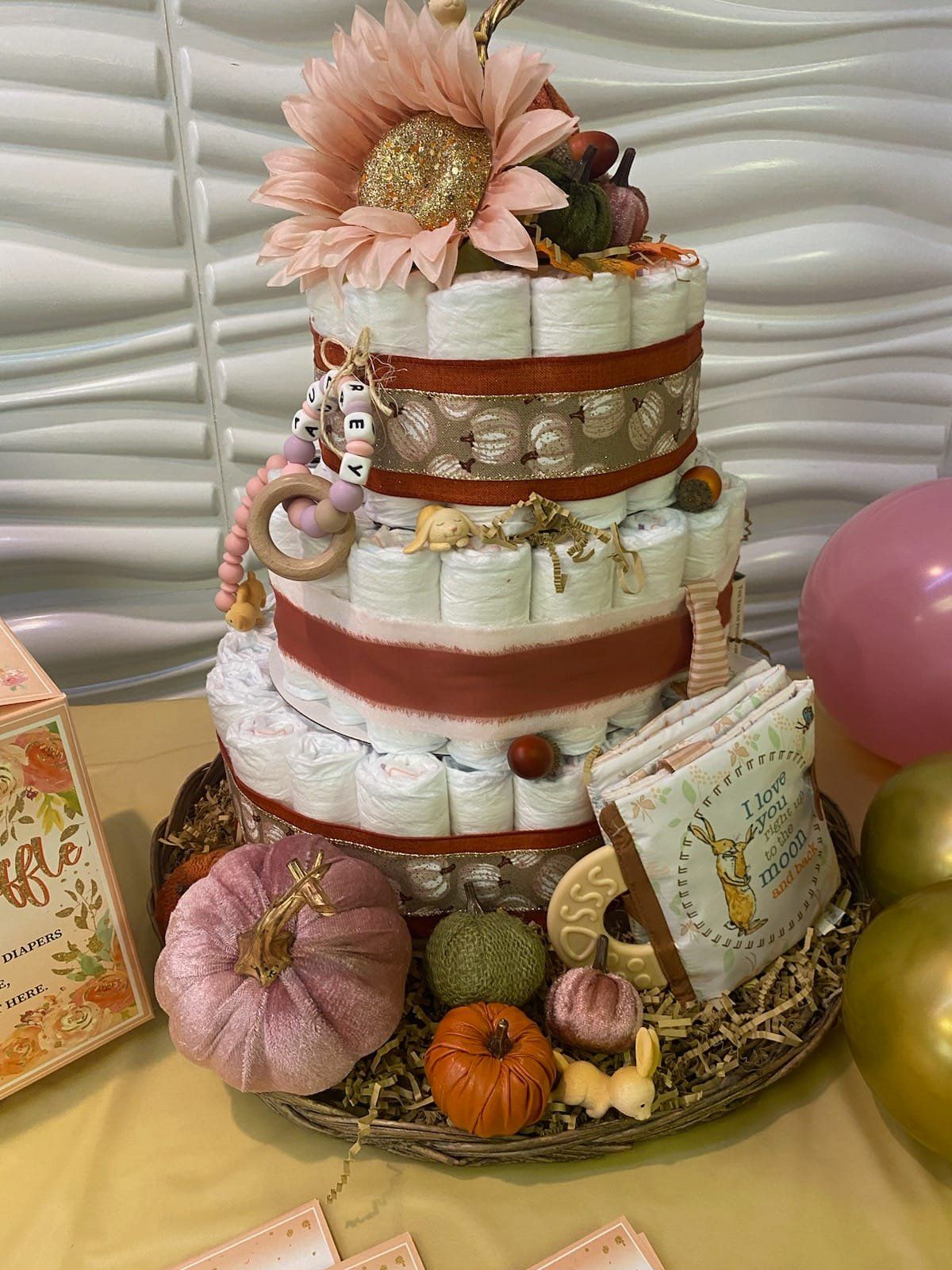 Diaper cake with autumn decorations: pumpkins, flowers, and a beaded teething ring.