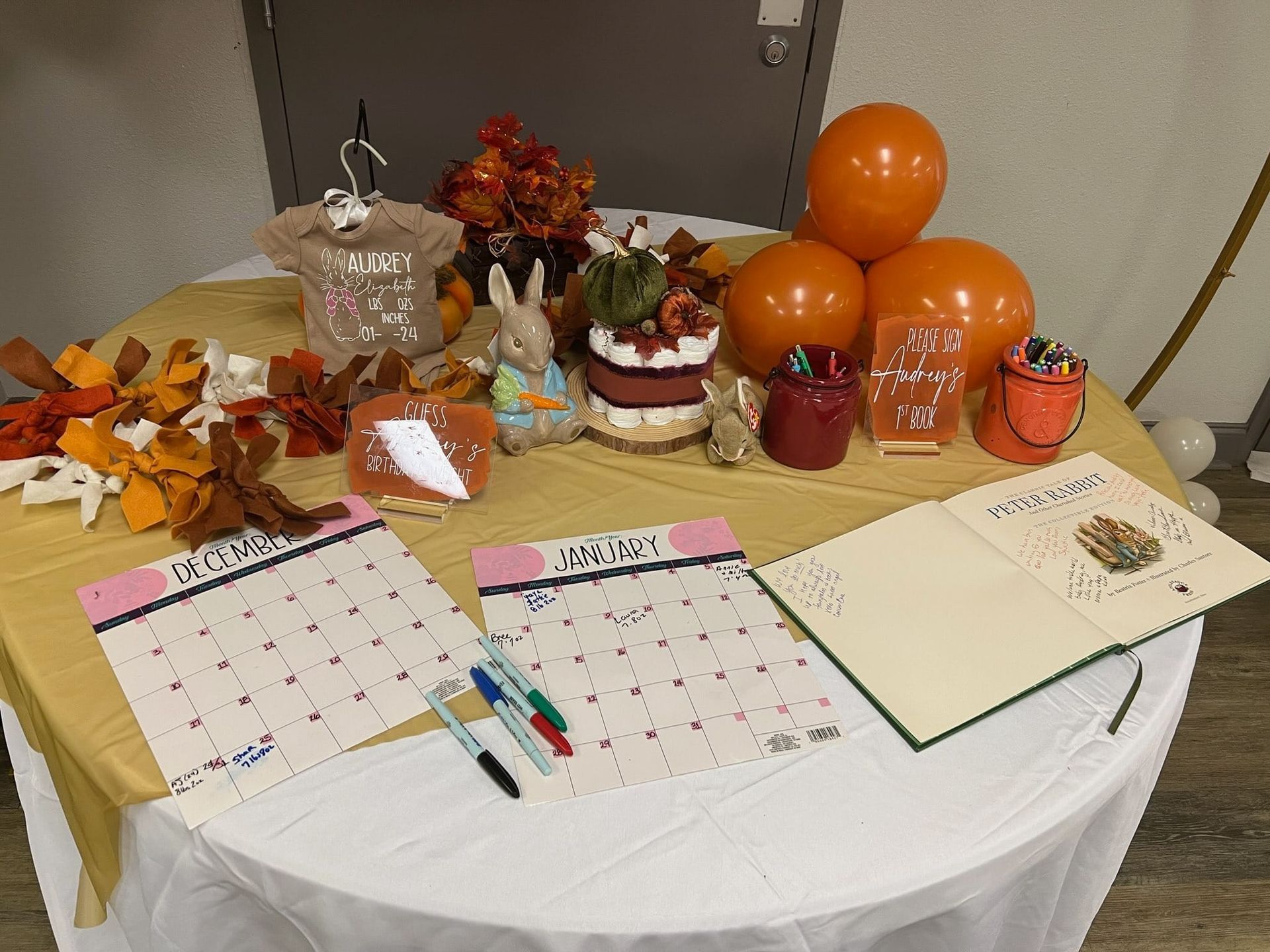 A table decorated with fall-themed items: balloons, cake, calendars, and a guest book.