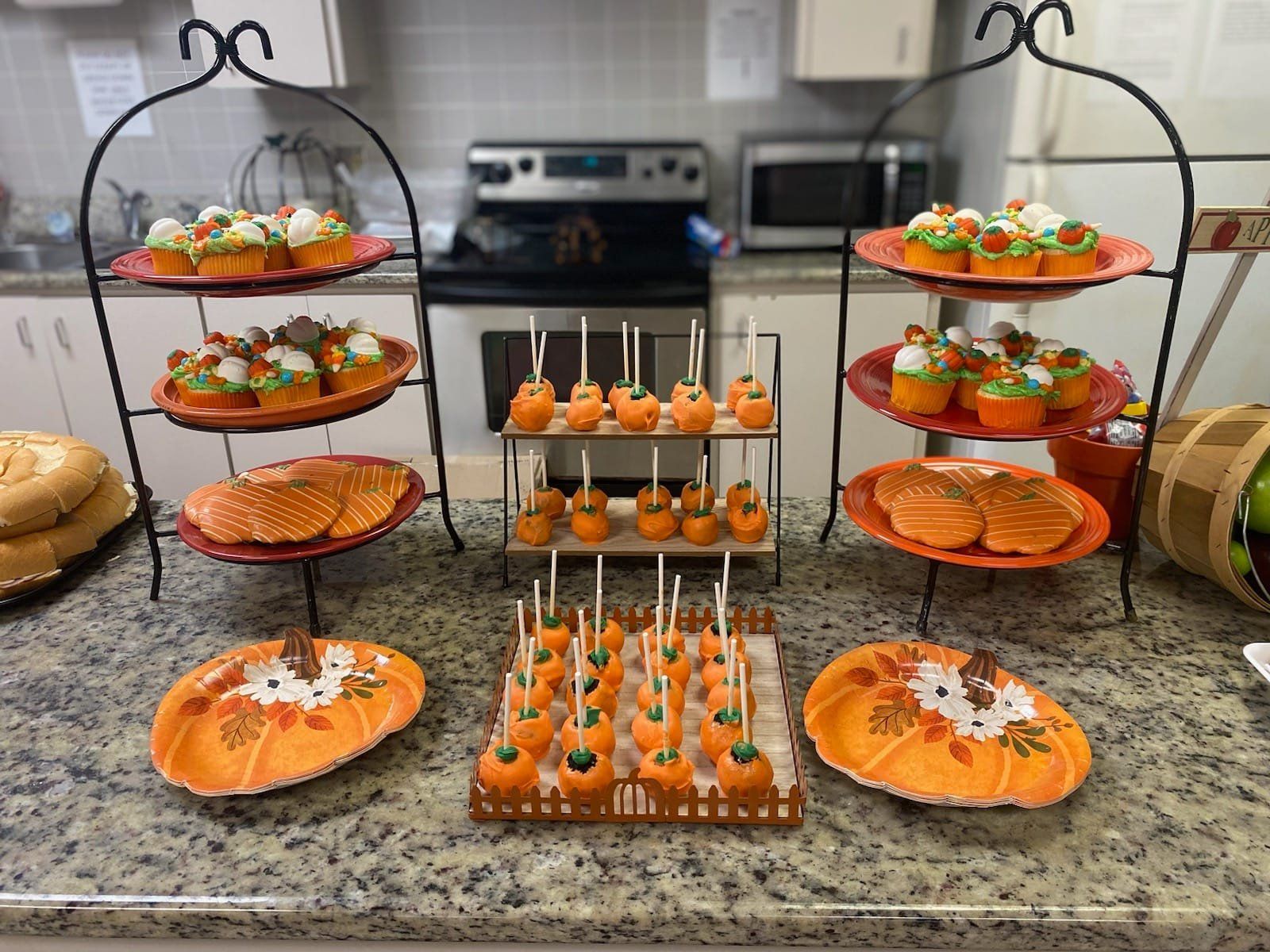 Dessert display with cupcakes, cake pops, and cookies, all orange and autumn themed, on tiered stands.