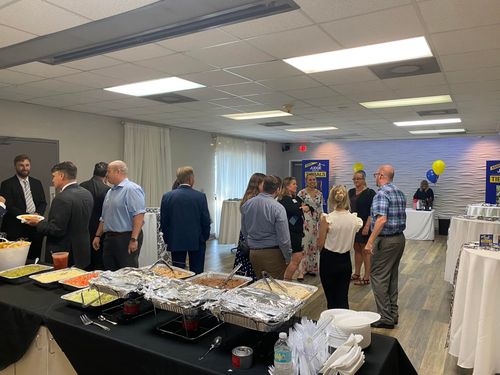 People at a business event with food spread. Indoors. Black tables with food, white tablecloths.