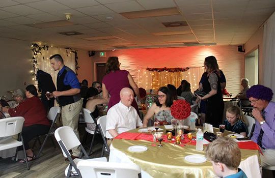People at a celebration; tables set with gold linens and centerpieces, some guests are standing and talking.