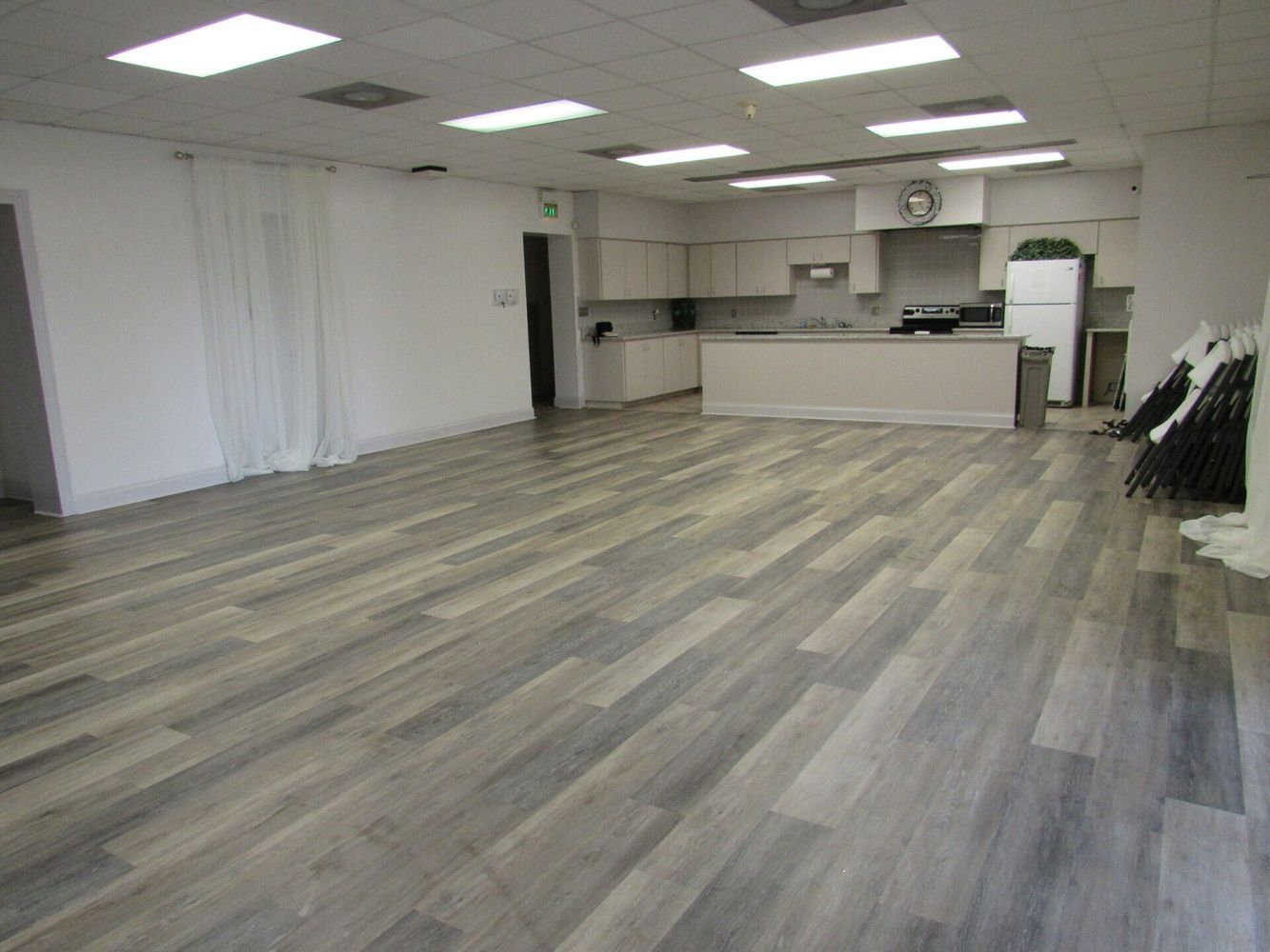 Empty room with hardwood floors, a kitchen, and bright overhead lights.