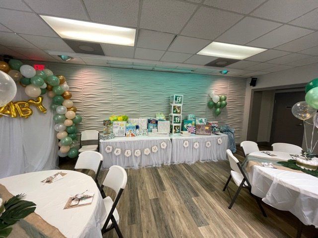 Baby shower party with balloon arch, gift table, white tables, and chairs.