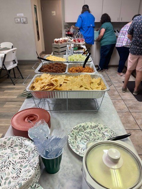 Food buffet with people serving themselves. Tacos and toppings are displayed.