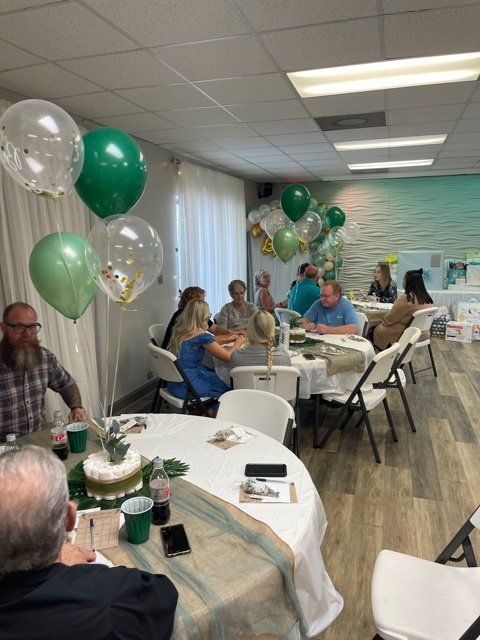 People seated at tables decorated with green balloons and decor at an event.
