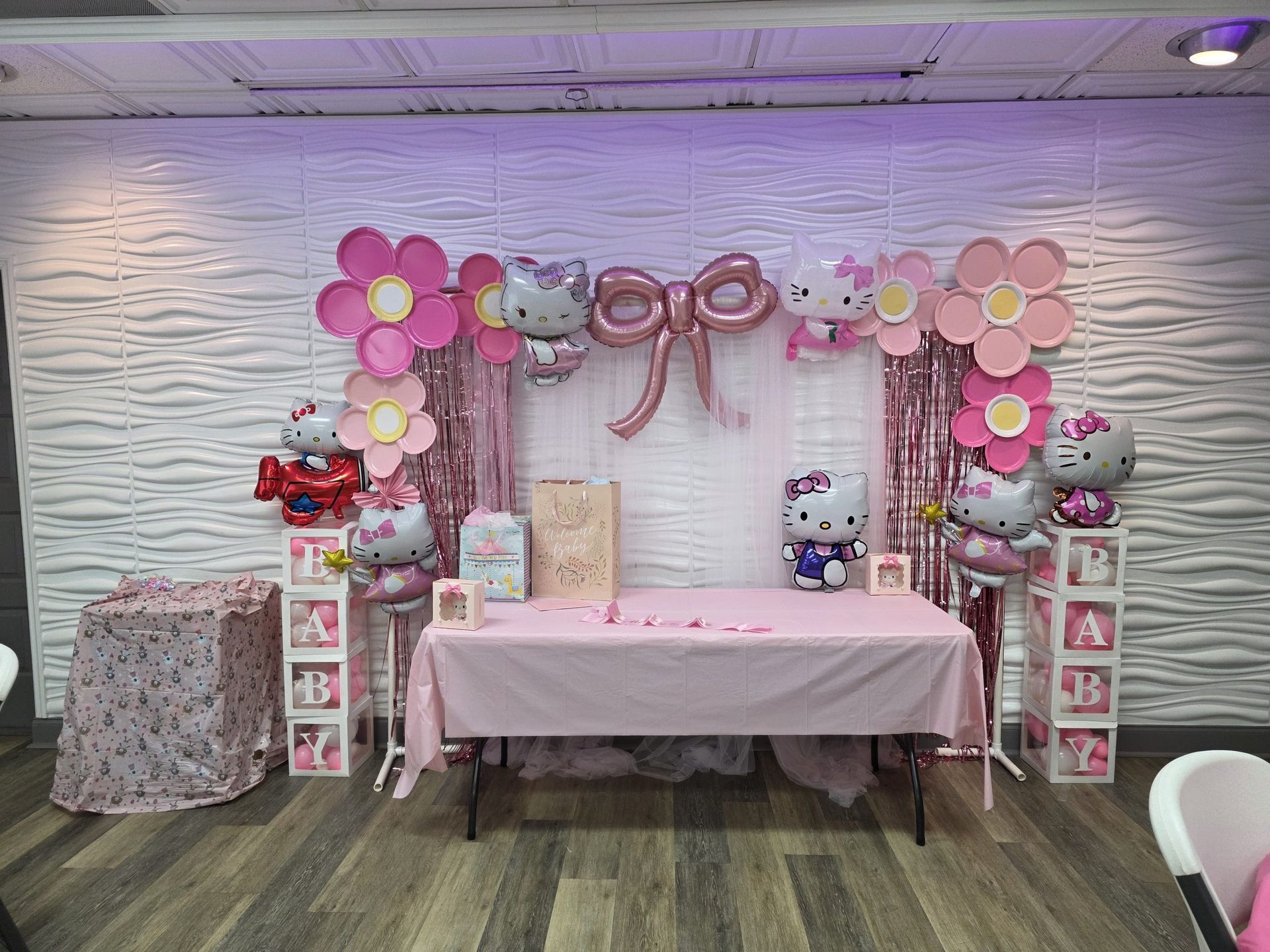 Hello Kitty-themed party backdrop. Pink decorations with balloons, flowers, and a table.