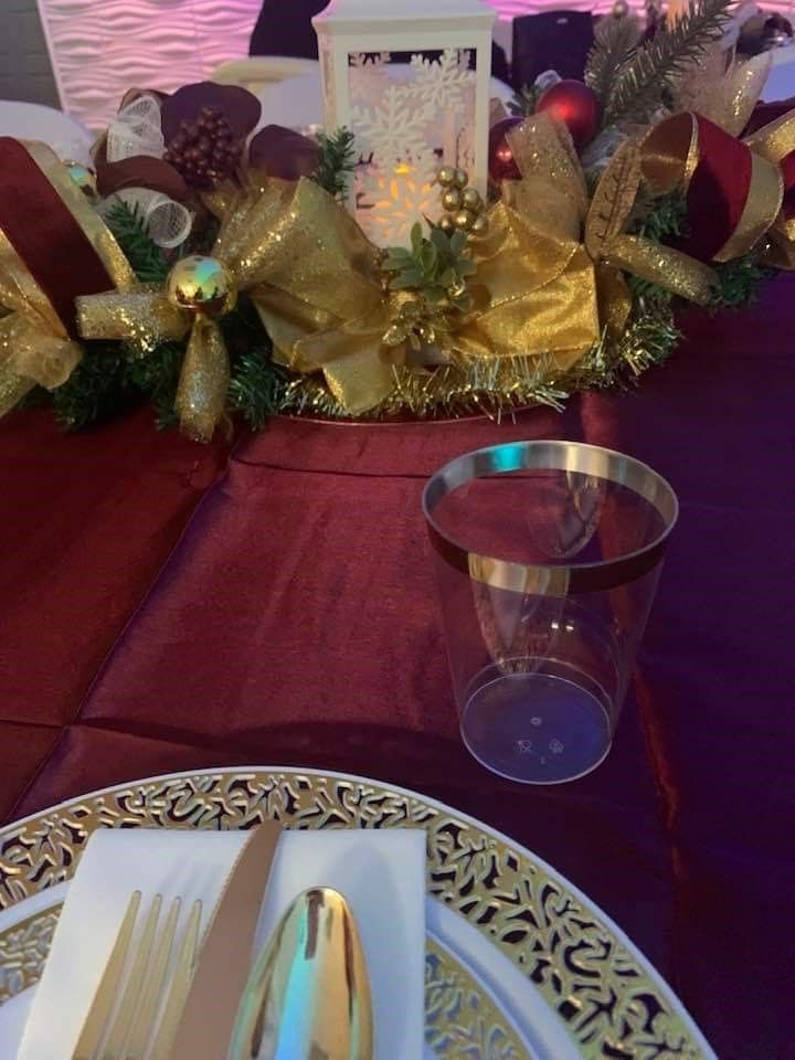 Festive table setting with gold and burgundy decor, including a centerpiece and place setting.