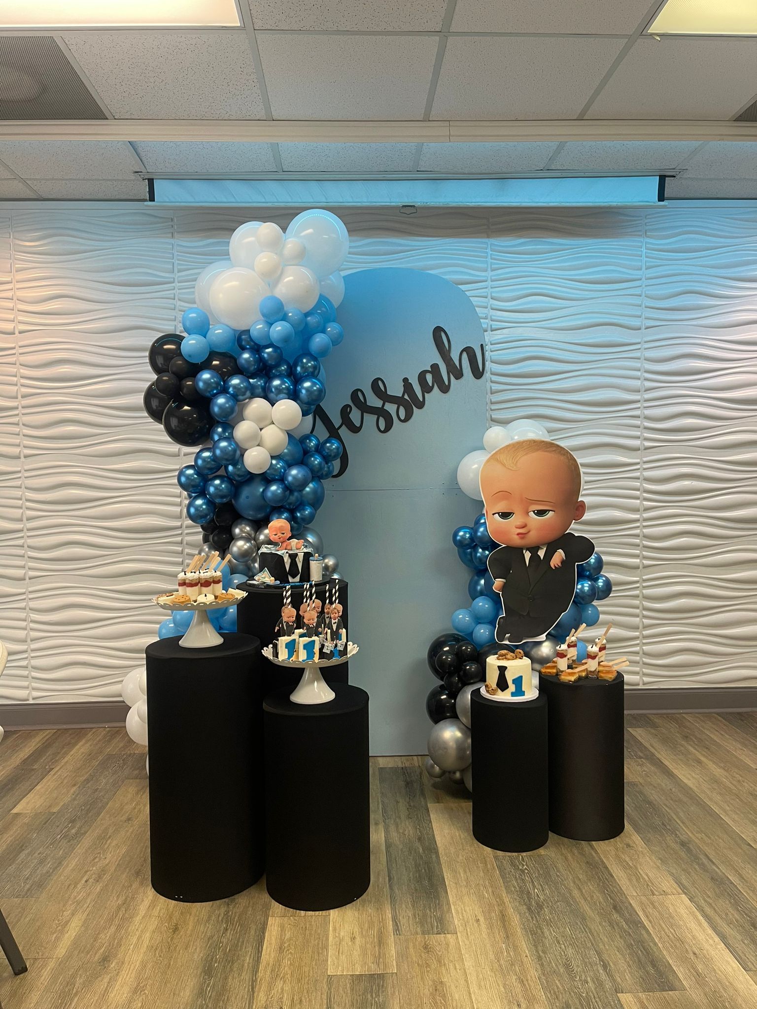 Boss Baby-themed party setup with balloon arches, cakes on black pedestals, and a wall backdrop.