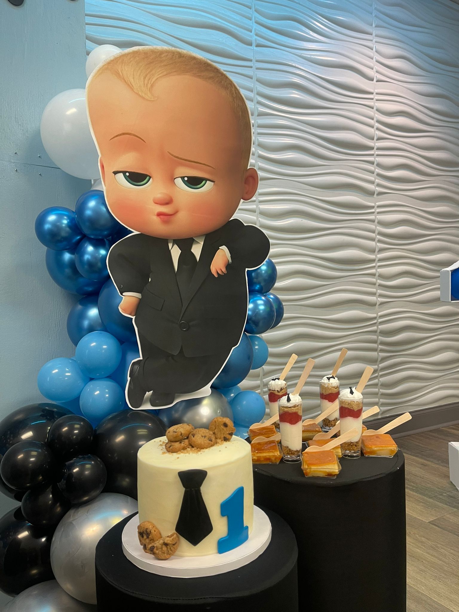 Boss Baby-themed party with cake, balloons, treats, and cutout figure.