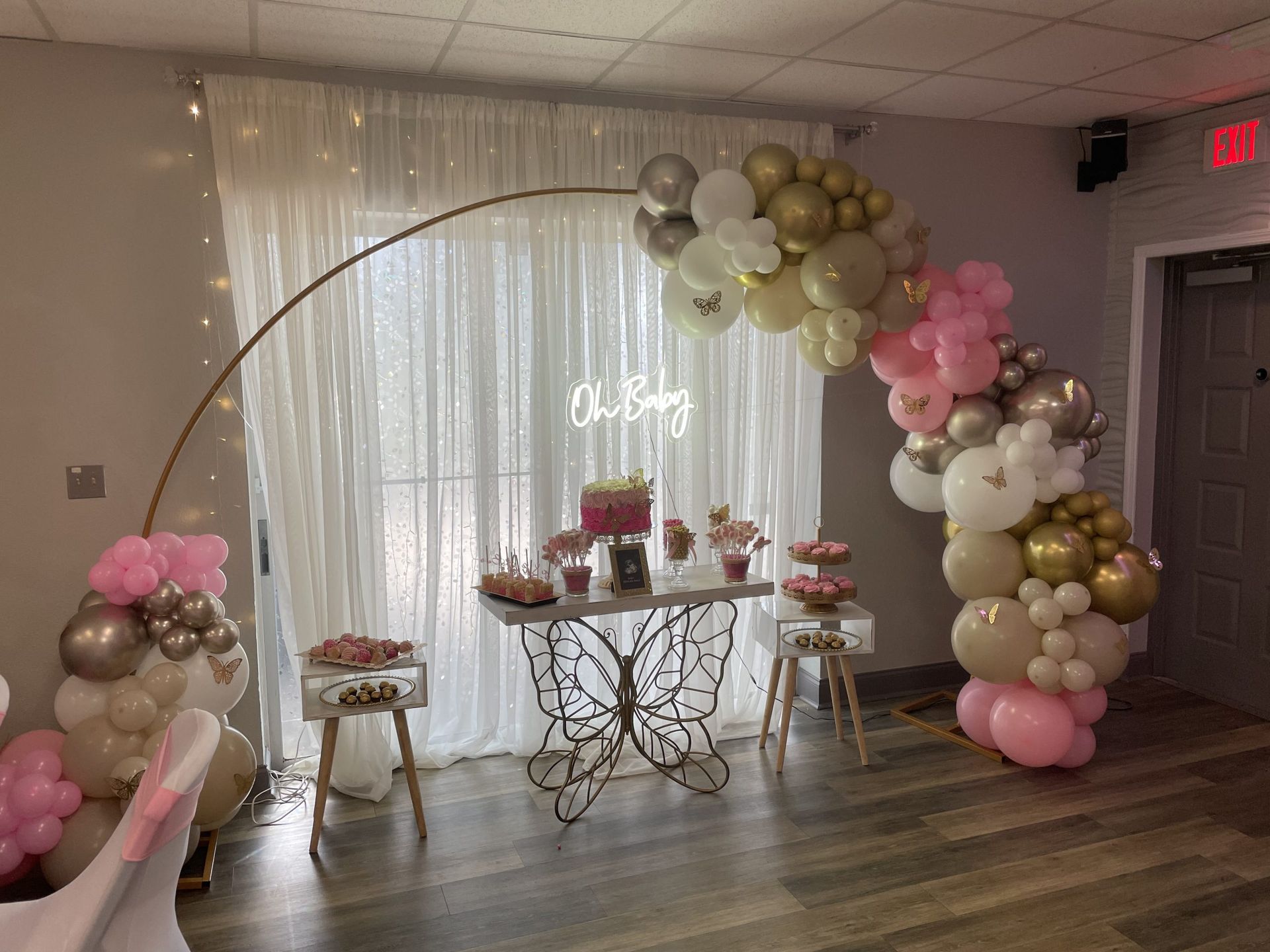 Baby shower with pink and gold balloon arch, table, and decorations.
