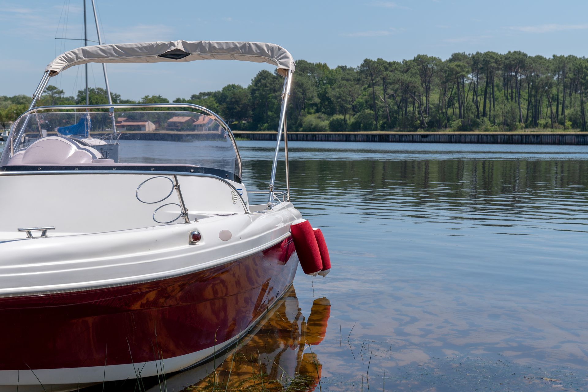White and red boat on calm water; trees in the background.