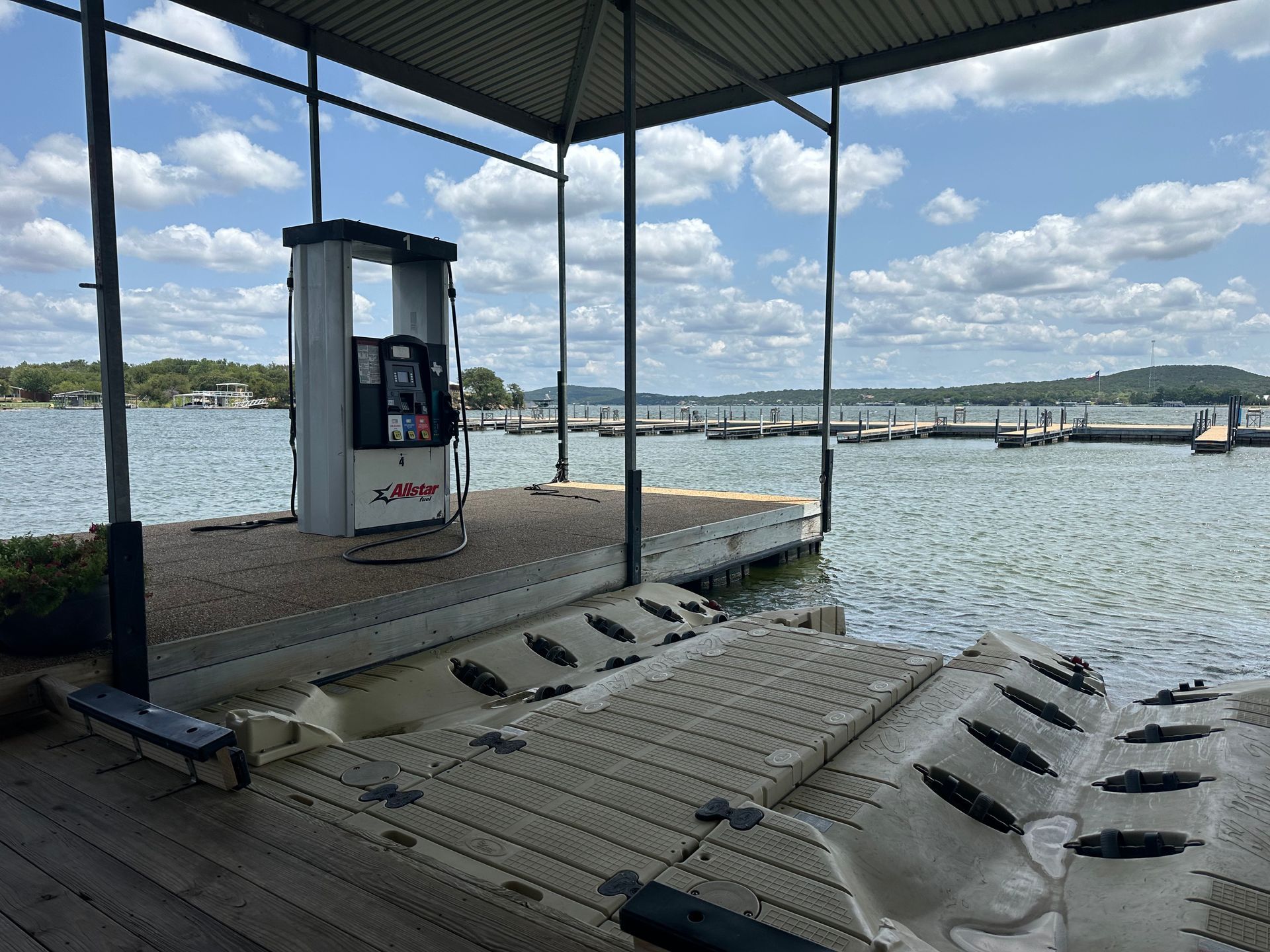 A gas pump is sitting on a dock next to a body of water.